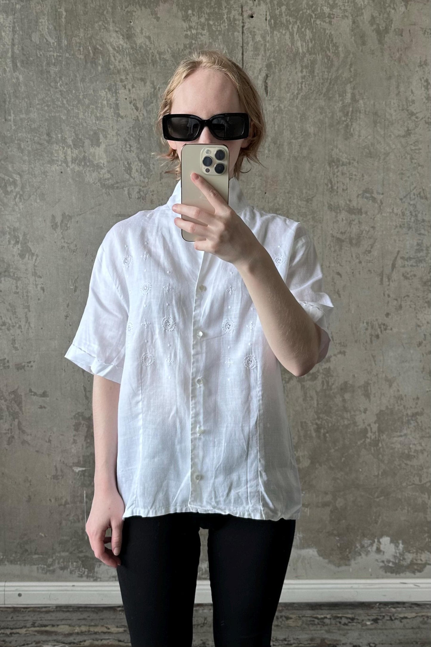 A person wearing a white shirt and sunglasses is taking a selfie with a smartphone.