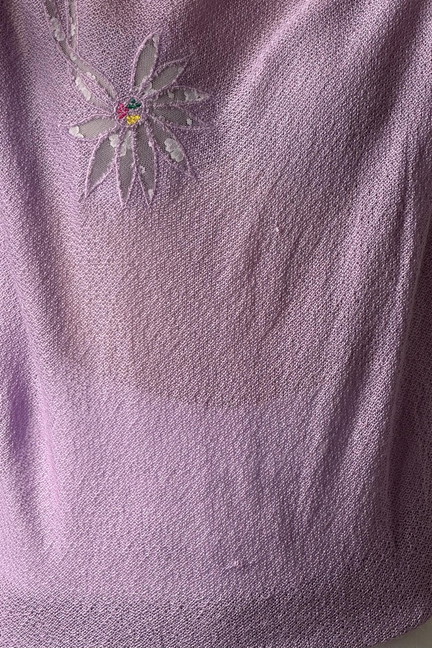 a close-up view of a soft, purple fabric with a delicate floral embroidered design on the left side.