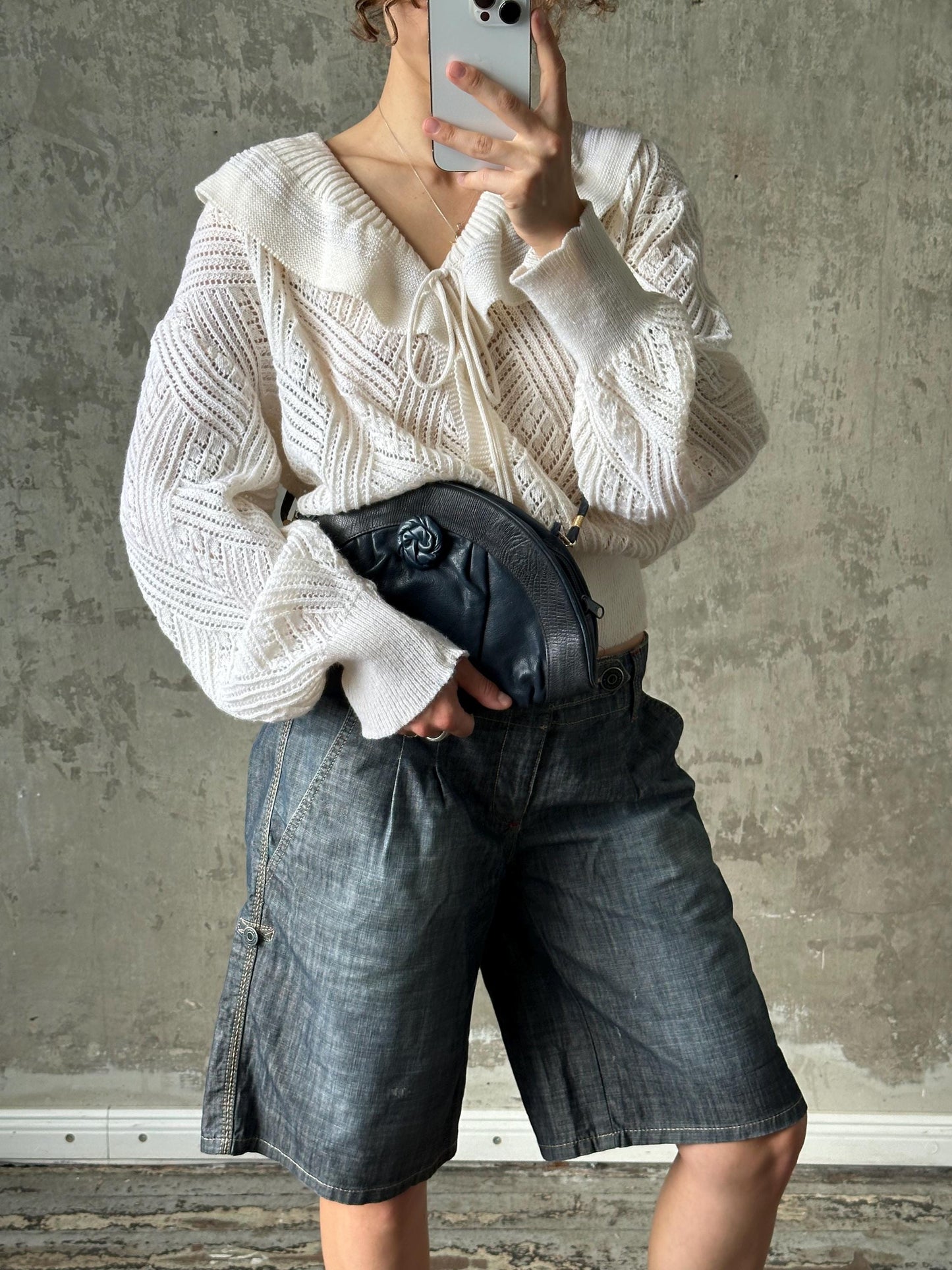 A person is taking a selfie with a white sweater, blue jeans, and a black purse.