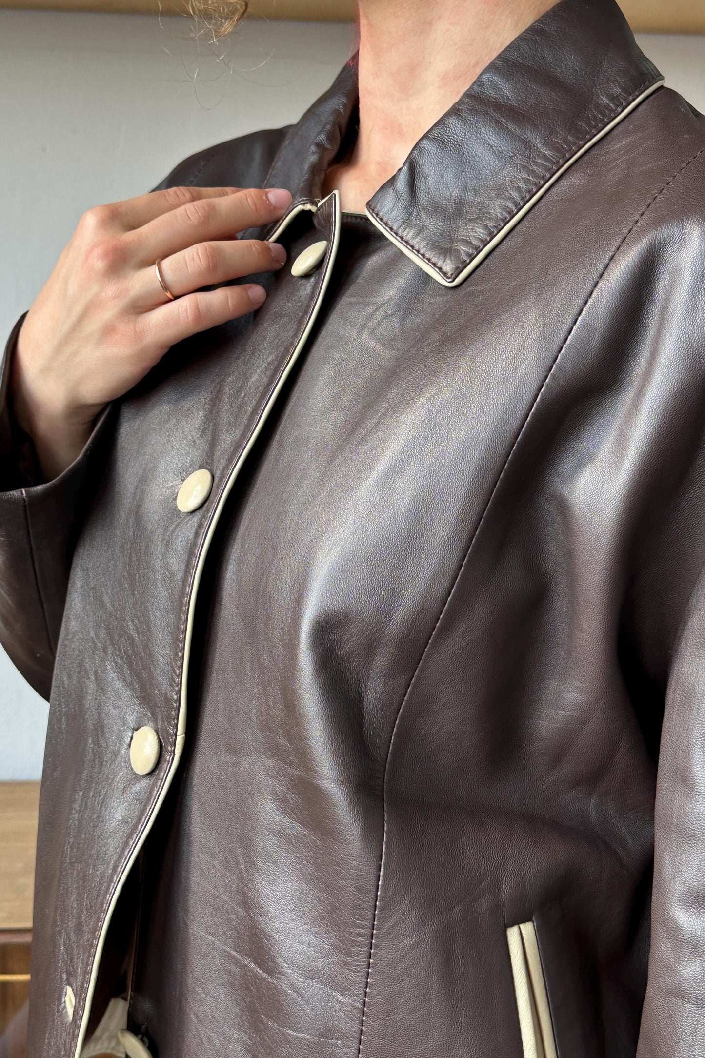 A close-up view of a person wearing a brown leather jacket with a white collar and buttons.