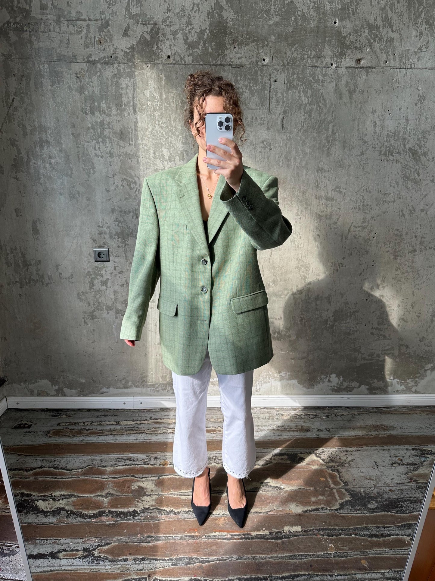 A person is taking a selfie in front of a concrete wall, holding a phone up to their face.