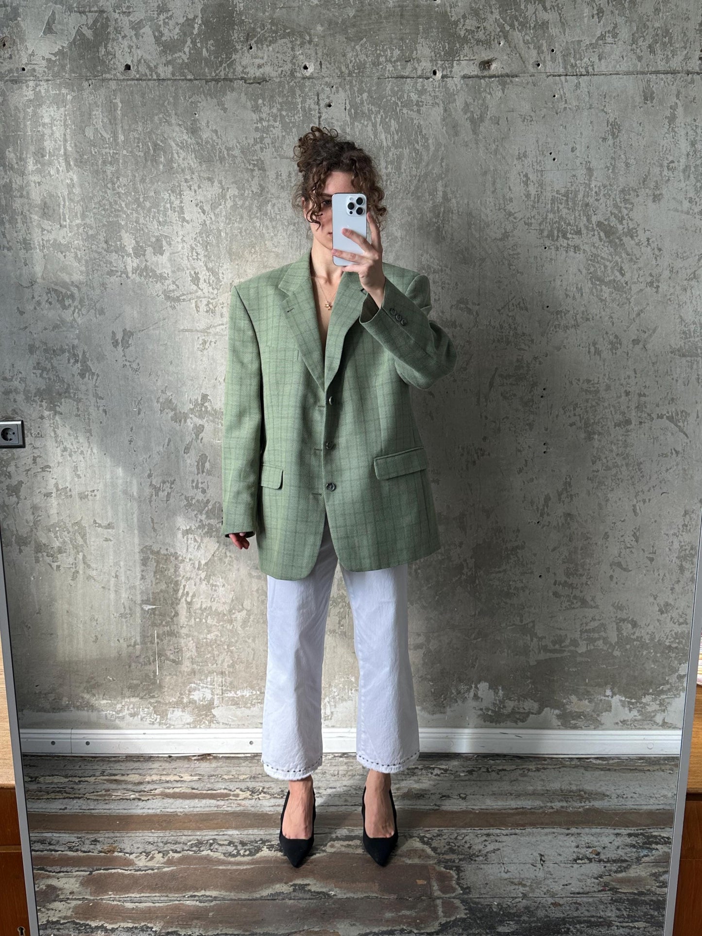 A person is taking a selfie in front of a concrete wall, holding a phone up to their face.