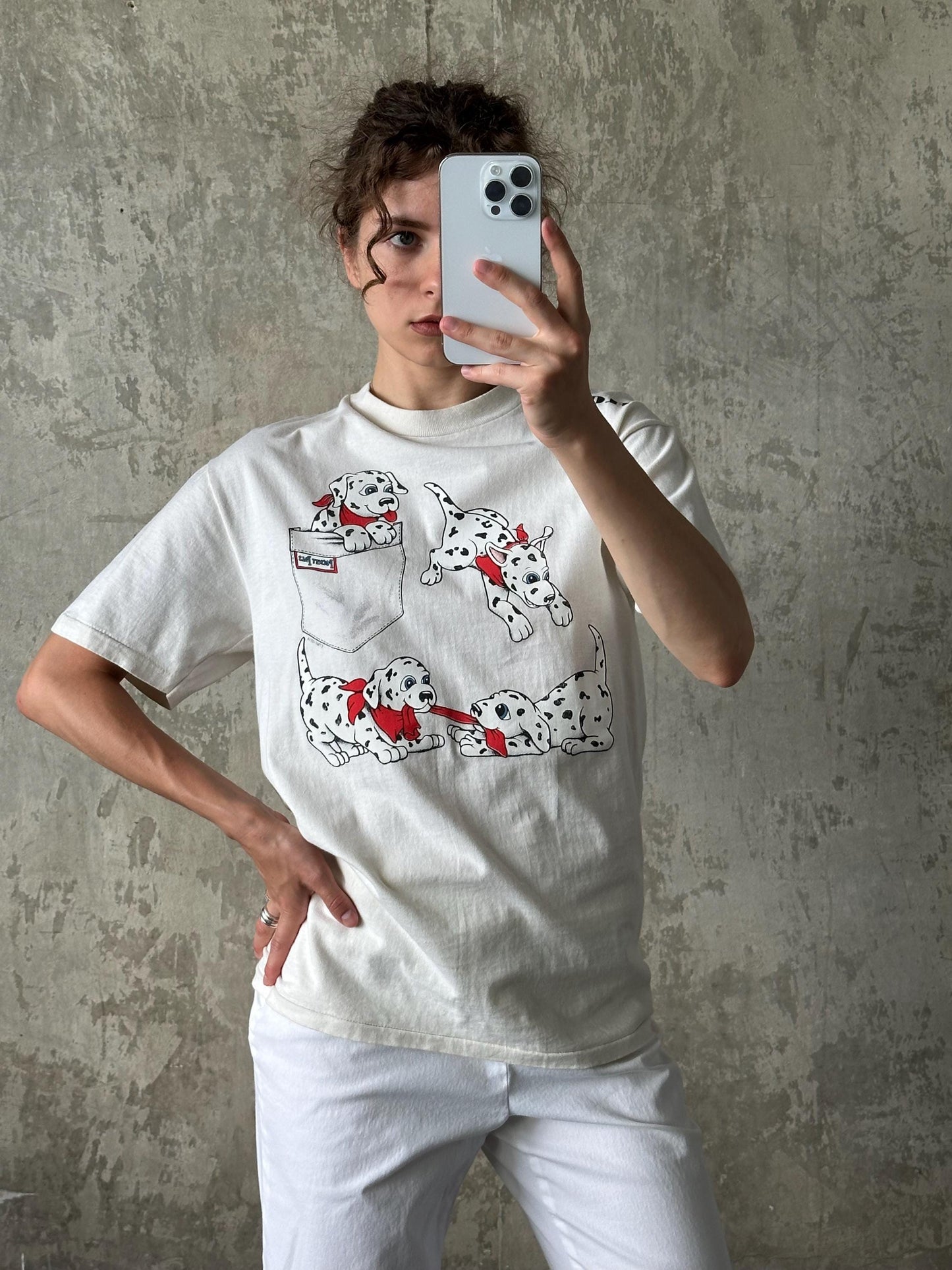 A person is taking a selfie with a smartphone, wearing a white t-shirt with a Dalmatian dog graphic.