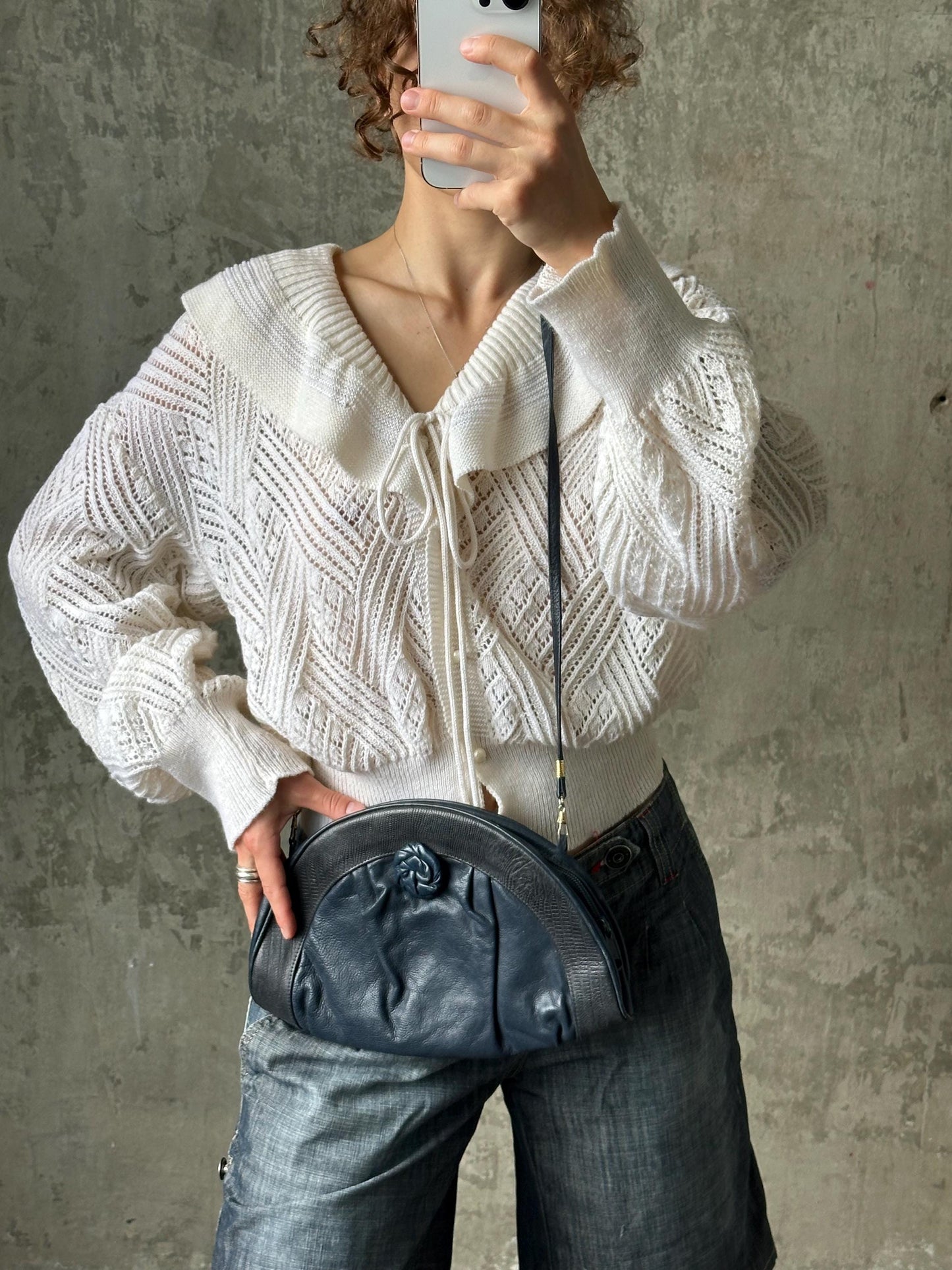 A person is taking a selfie with a white sweater and a black purse.
