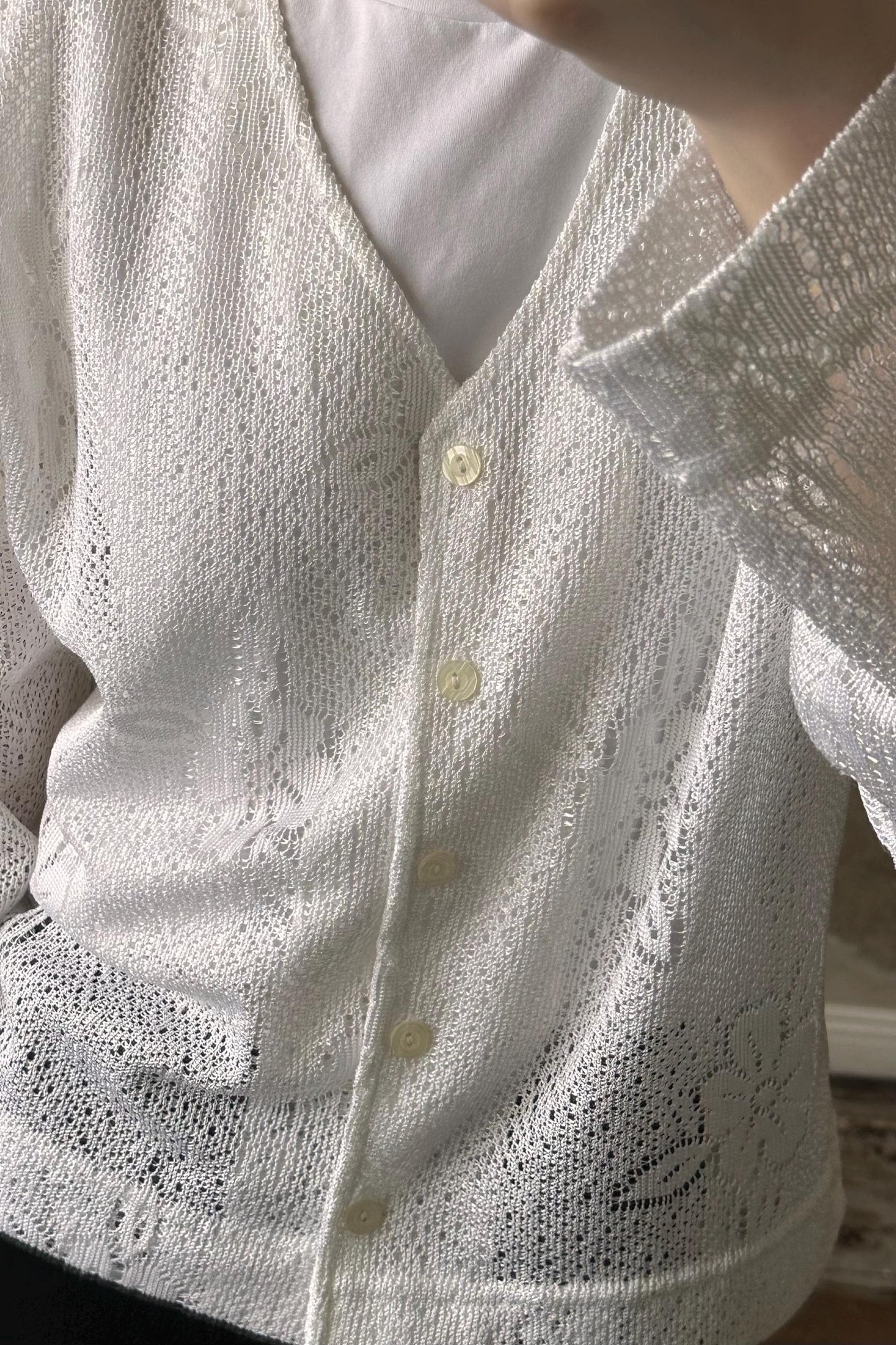 A close-up view of a white lace cardigan with three buttons, worn by a person.