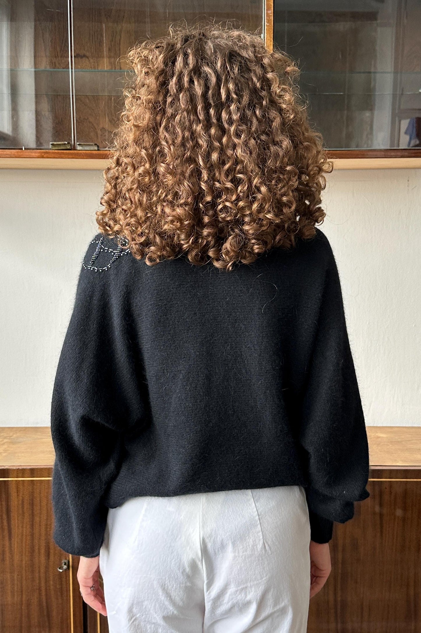 a person with curly hair wearing a black sweater and white pants, facing away from the camera.