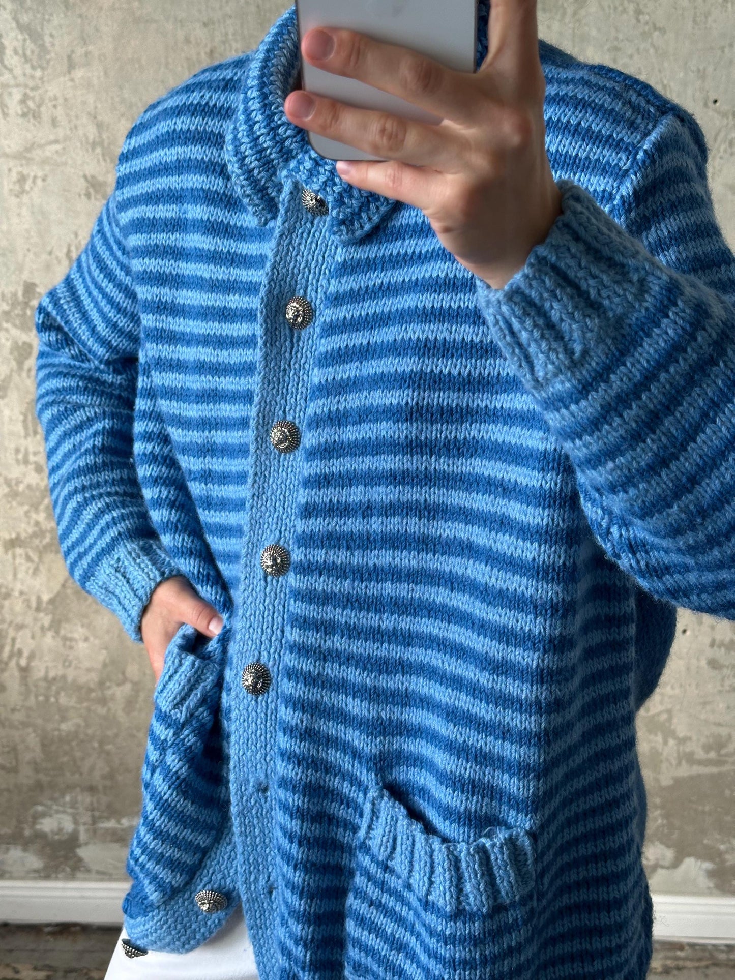 A person is taking a selfie with a blue and white striped cardigan, holding a phone up to their face.