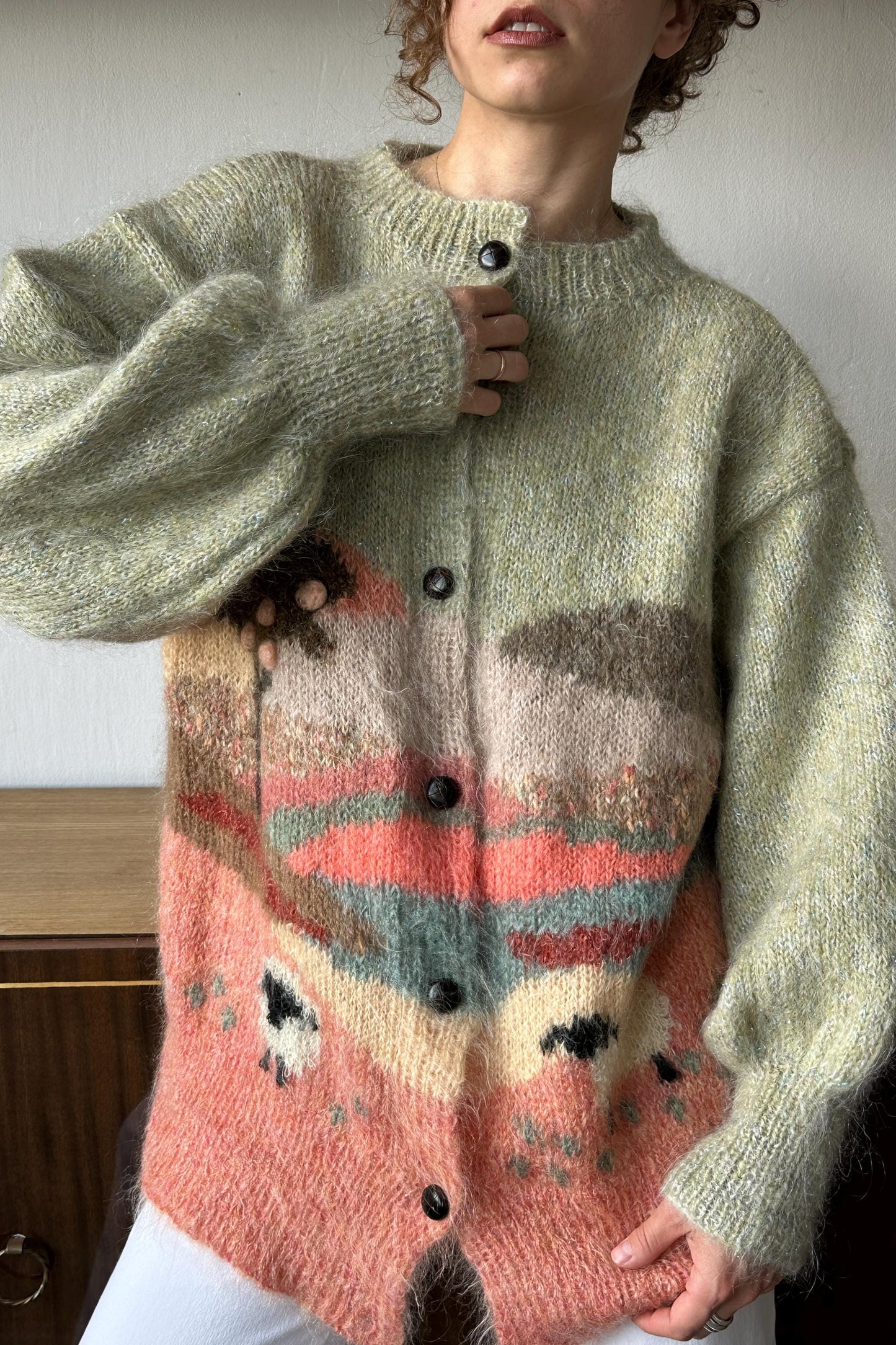 A person wearing a gray cardigan with a colorful, abstract pattern on the front.