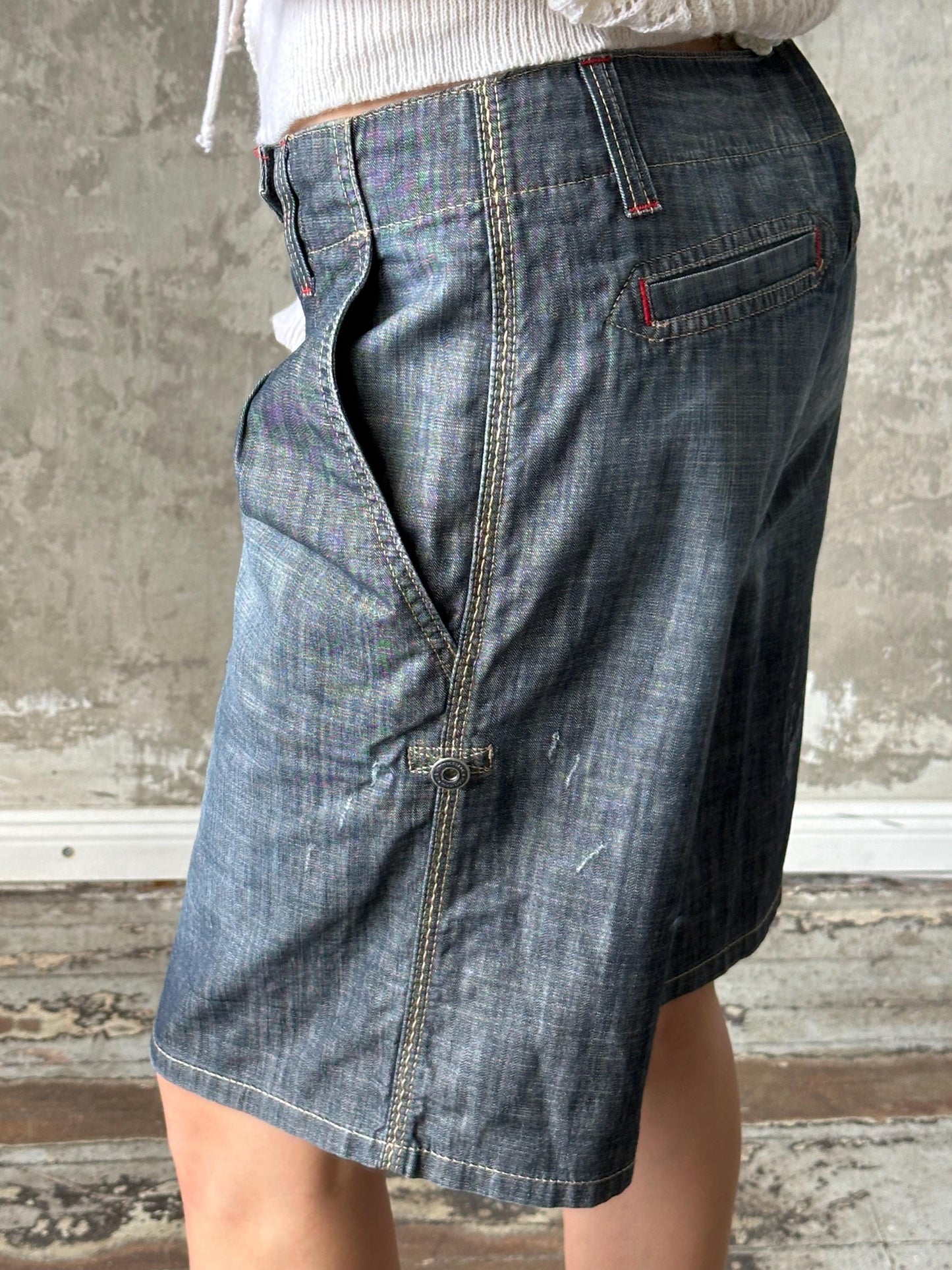A person wearing a denim skirt with a zipper detail and a pocket.