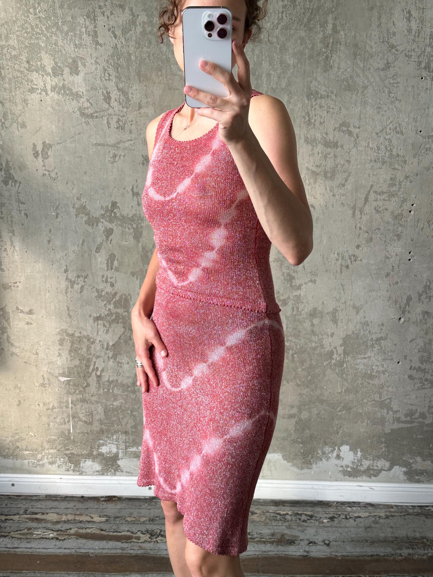A woman is taking a selfie with her phone, wearing a pink dress with a tie-dye pattern.