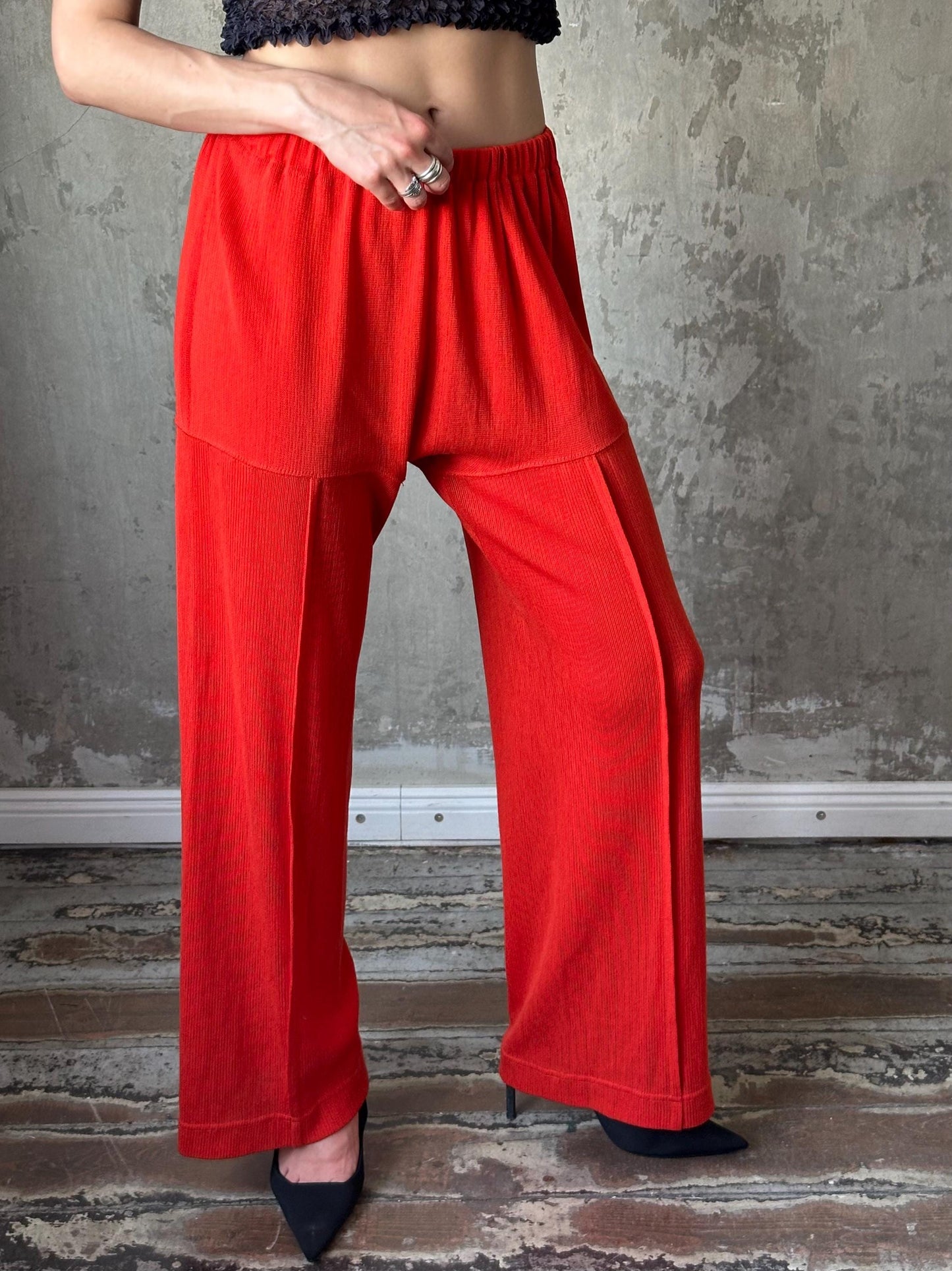 A person wearing red pants and a black top stands in front of a concrete wall.