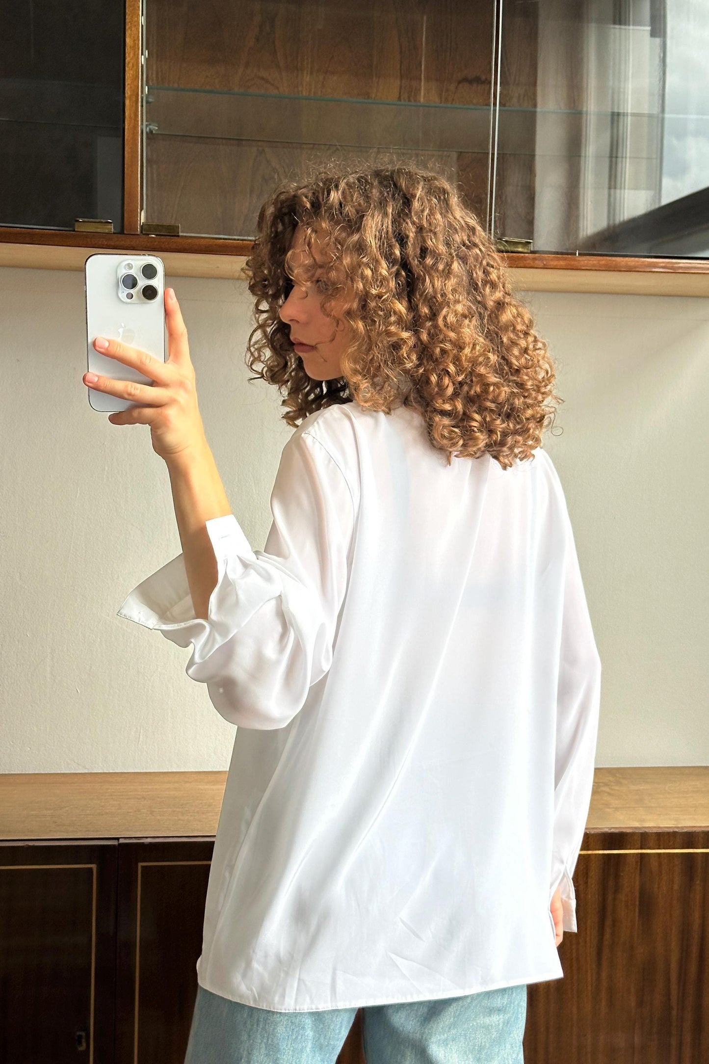 A woman with curly hair is taking a selfie with a smartphone, holding the device up to her face.
