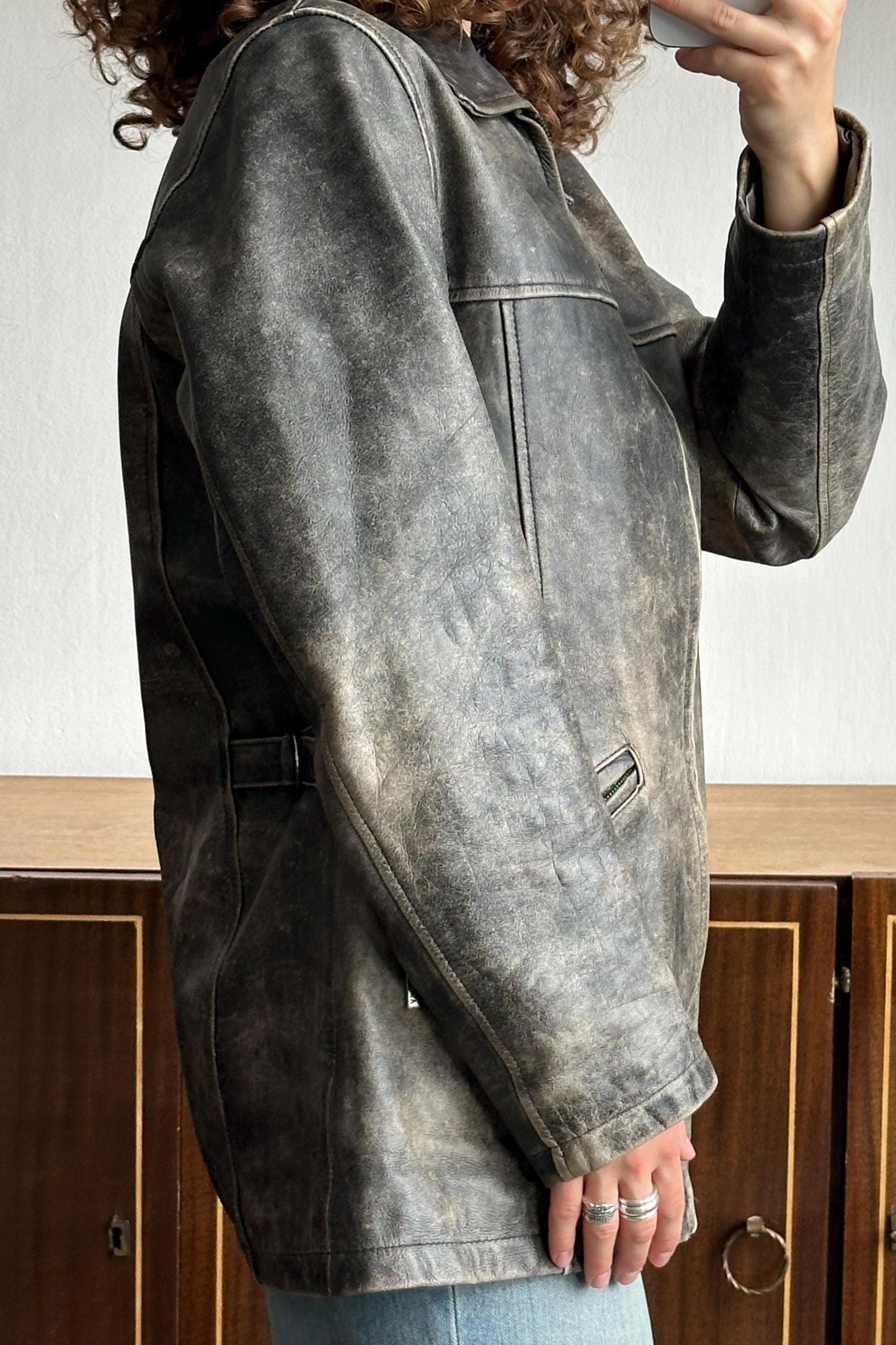 A person wearing a black leather jacket is taking a selfie with a white object in their hand.