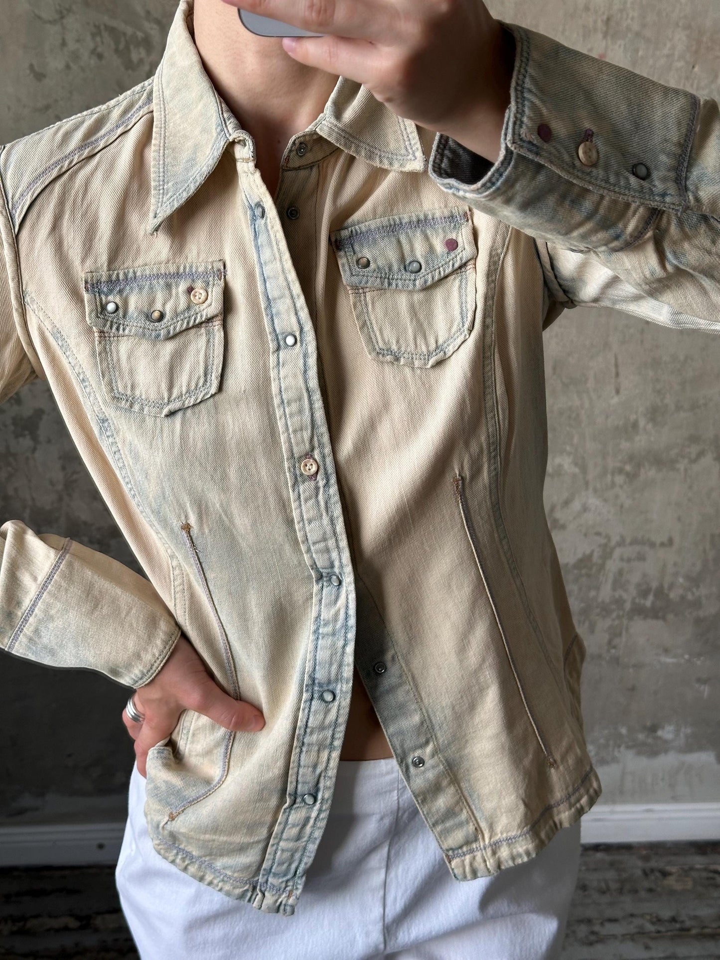 A person wearing a beige denim jacket with a button-down front and two pockets, standing in front of a concrete wall.