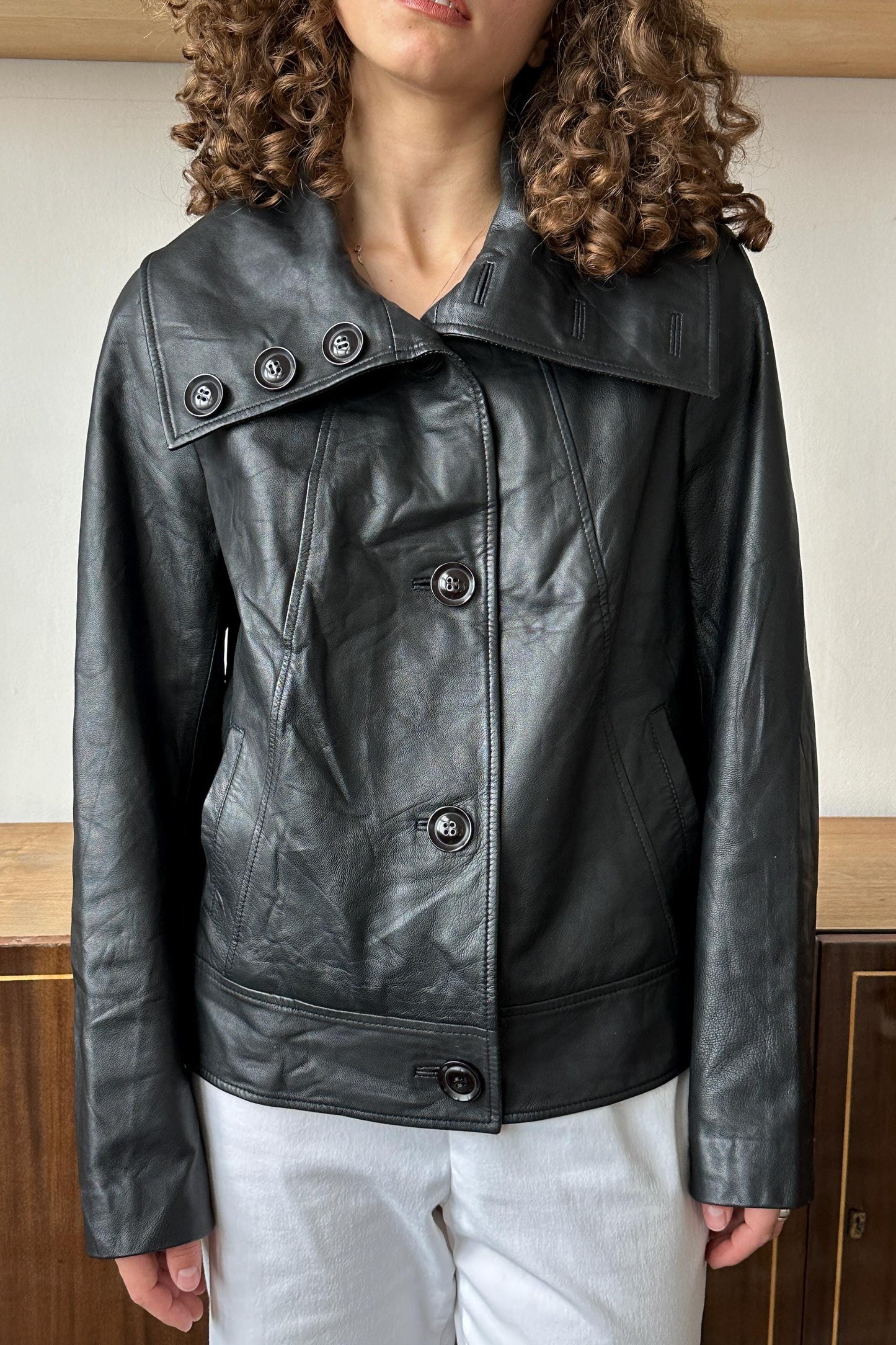 A woman wearing a black leather jacket with a high collar and three buttons.