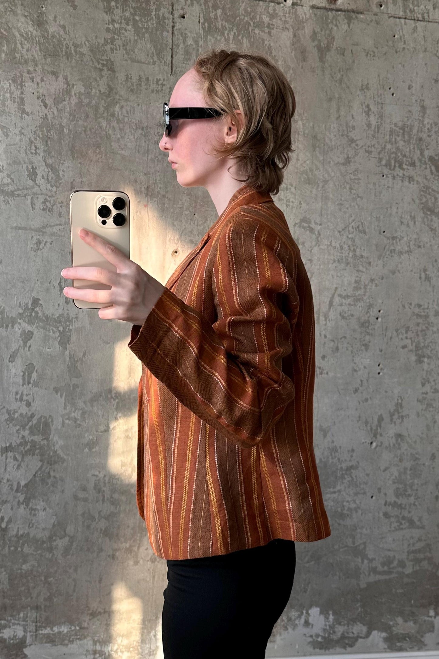 A person wearing a striped jacket and sunglasses is holding a smartphone and appears to be taking a photo or recording a video.