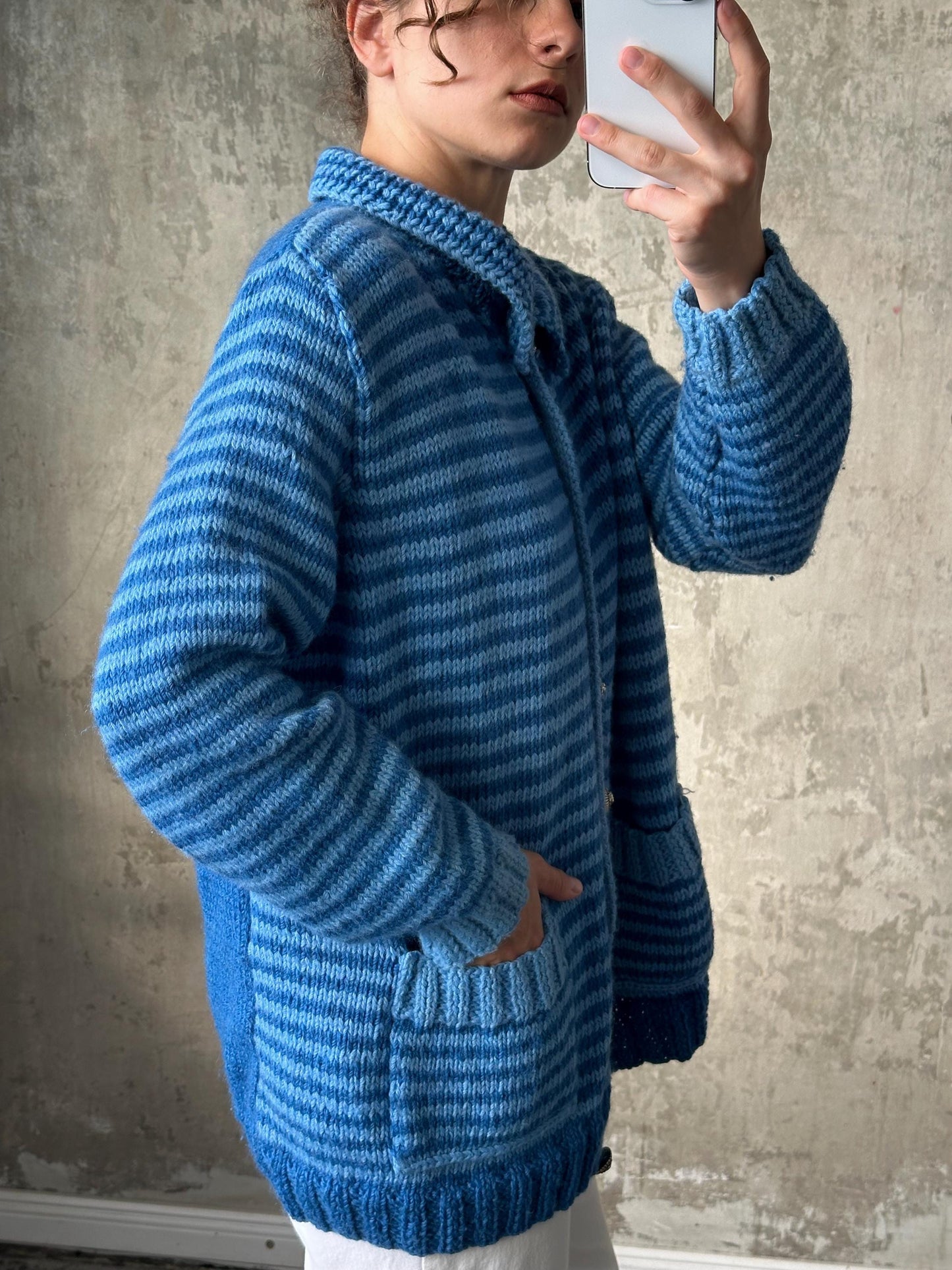 A person is taking a selfie with a blue and white striped sweater, holding a smartphone in their hand.