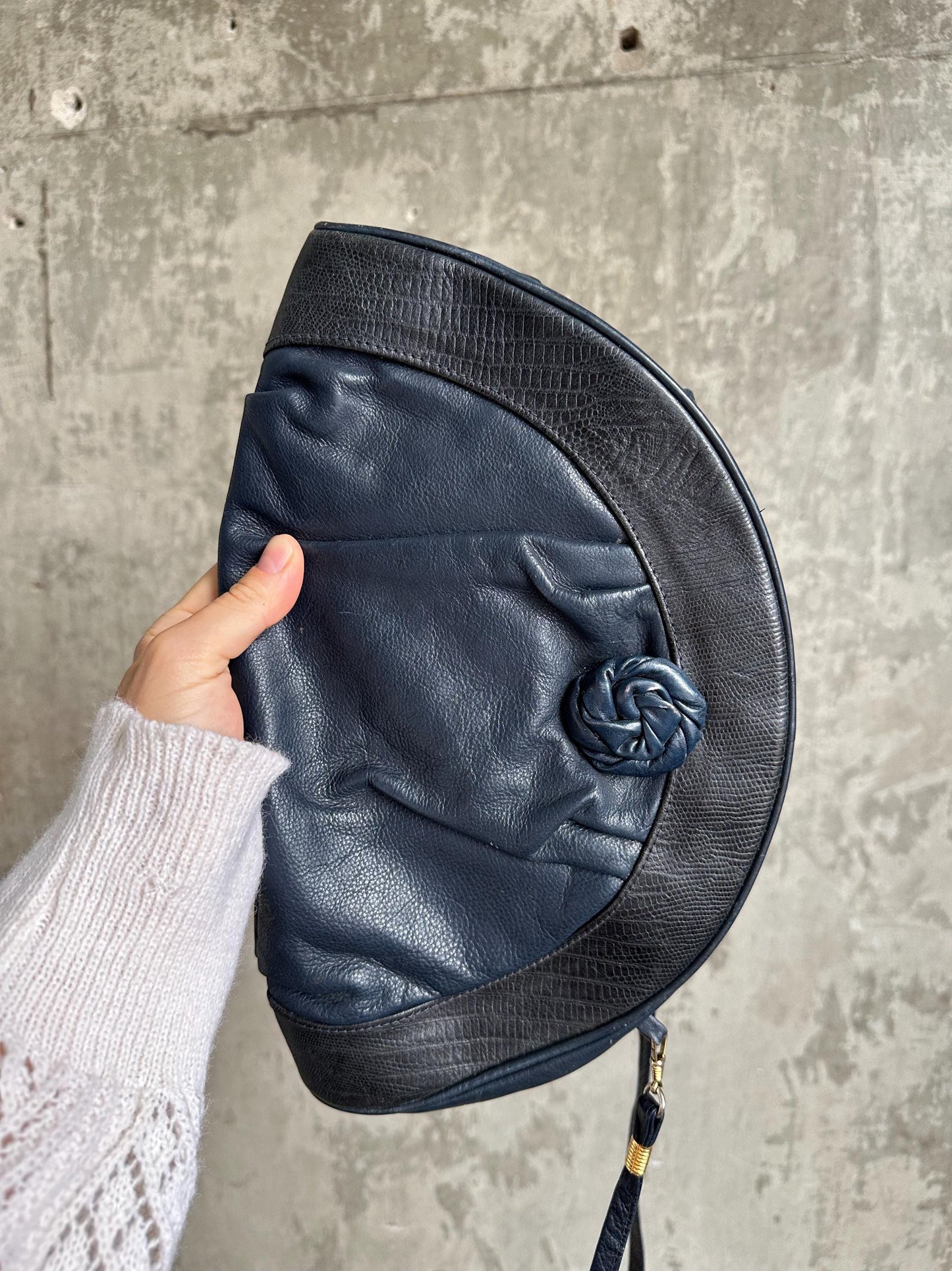 A hand holding a black leather purse with a twisted metal clasp.