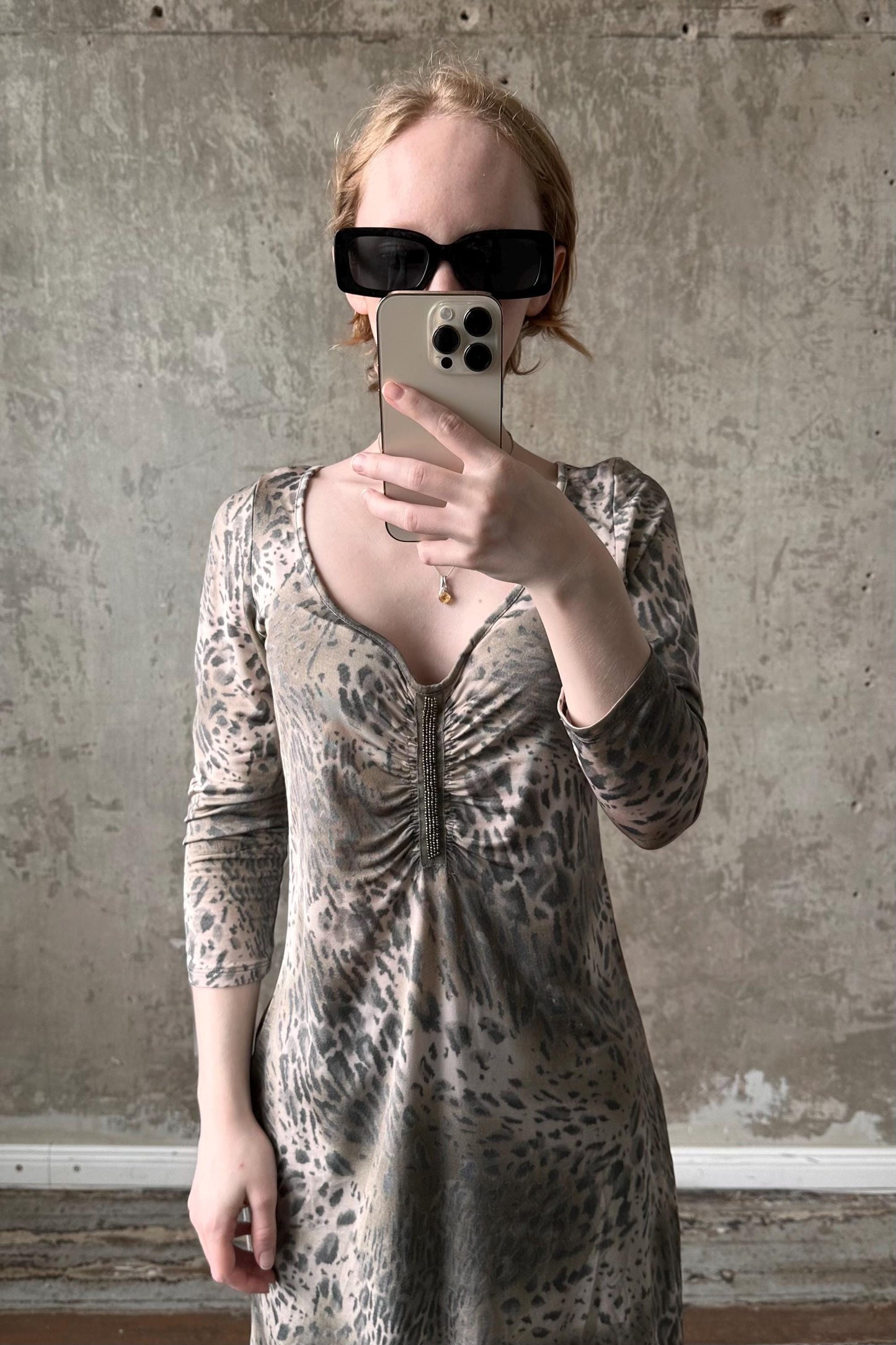 A woman wearing a leopard print dress and sunglasses is taking a selfie with her iPhone.