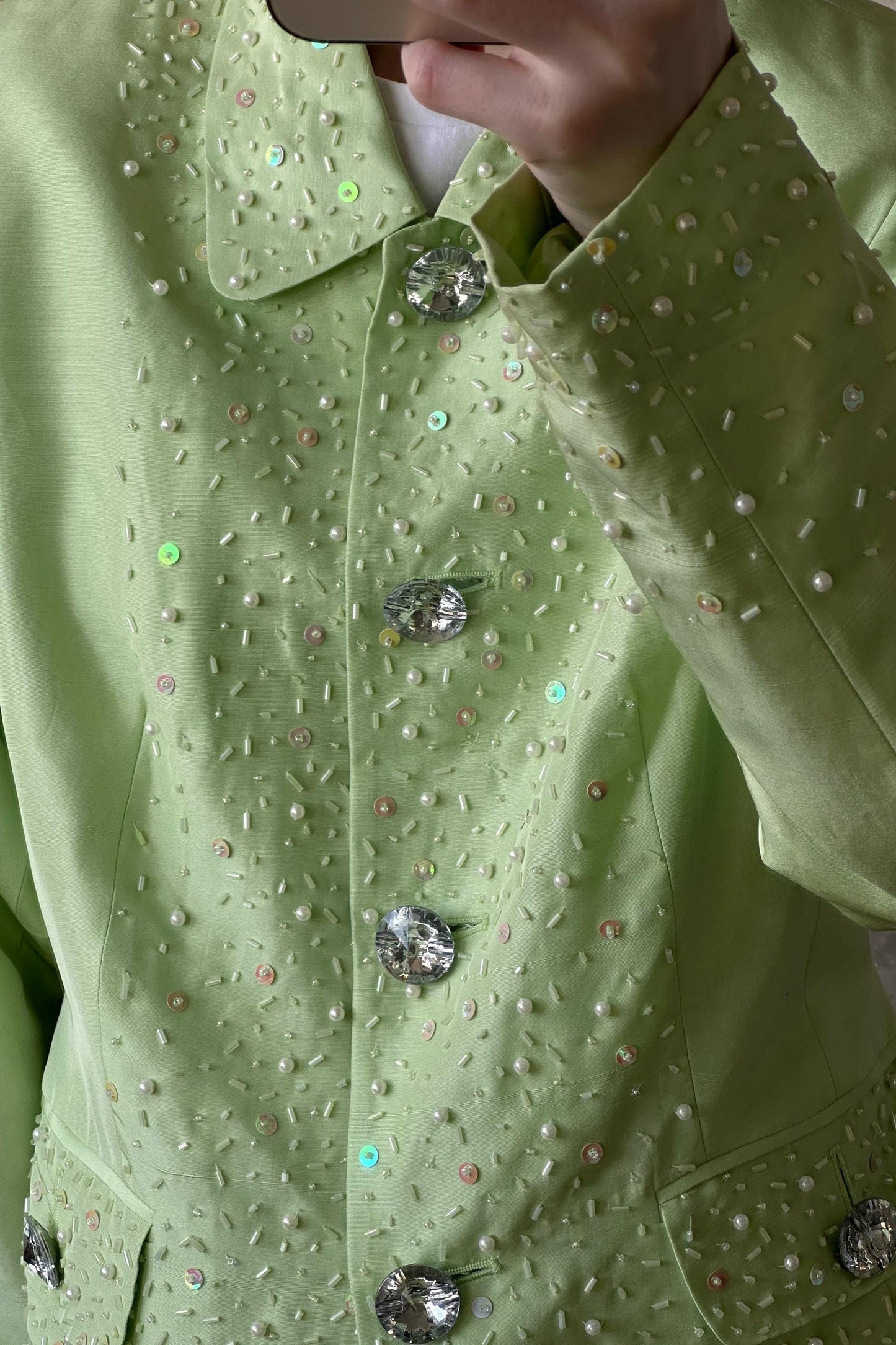 A close-up view of a person wearing a mint green jacket with sparkling embellishments, including buttons and sequins.