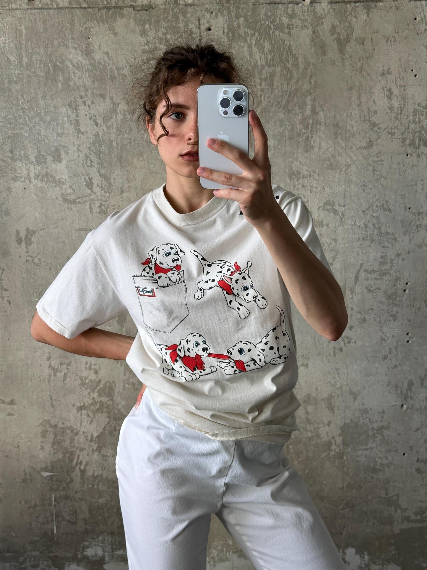 A person is taking a selfie with a smartphone, wearing a white t-shirt with a Dalmatian dog design.