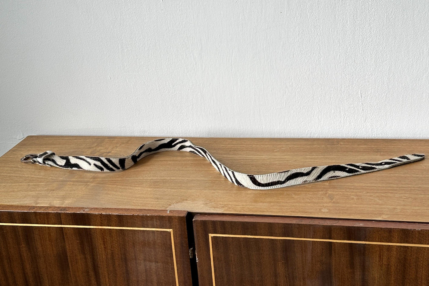 A zebra-striped belt is lying on a wooden surface, possibly a cabinet or dresser.