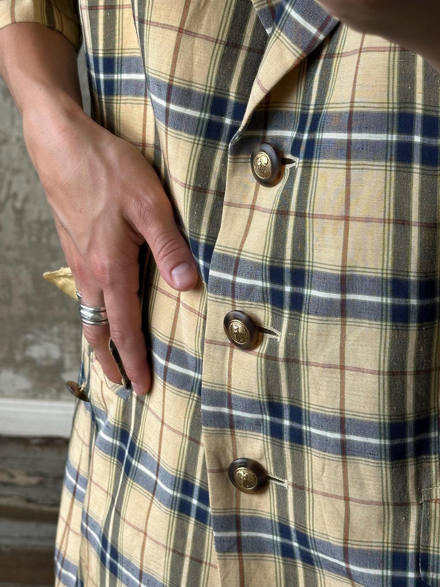 A close-up of a person's torso wearing a plaid shirt with buttons, and a hand resting on the pocket.