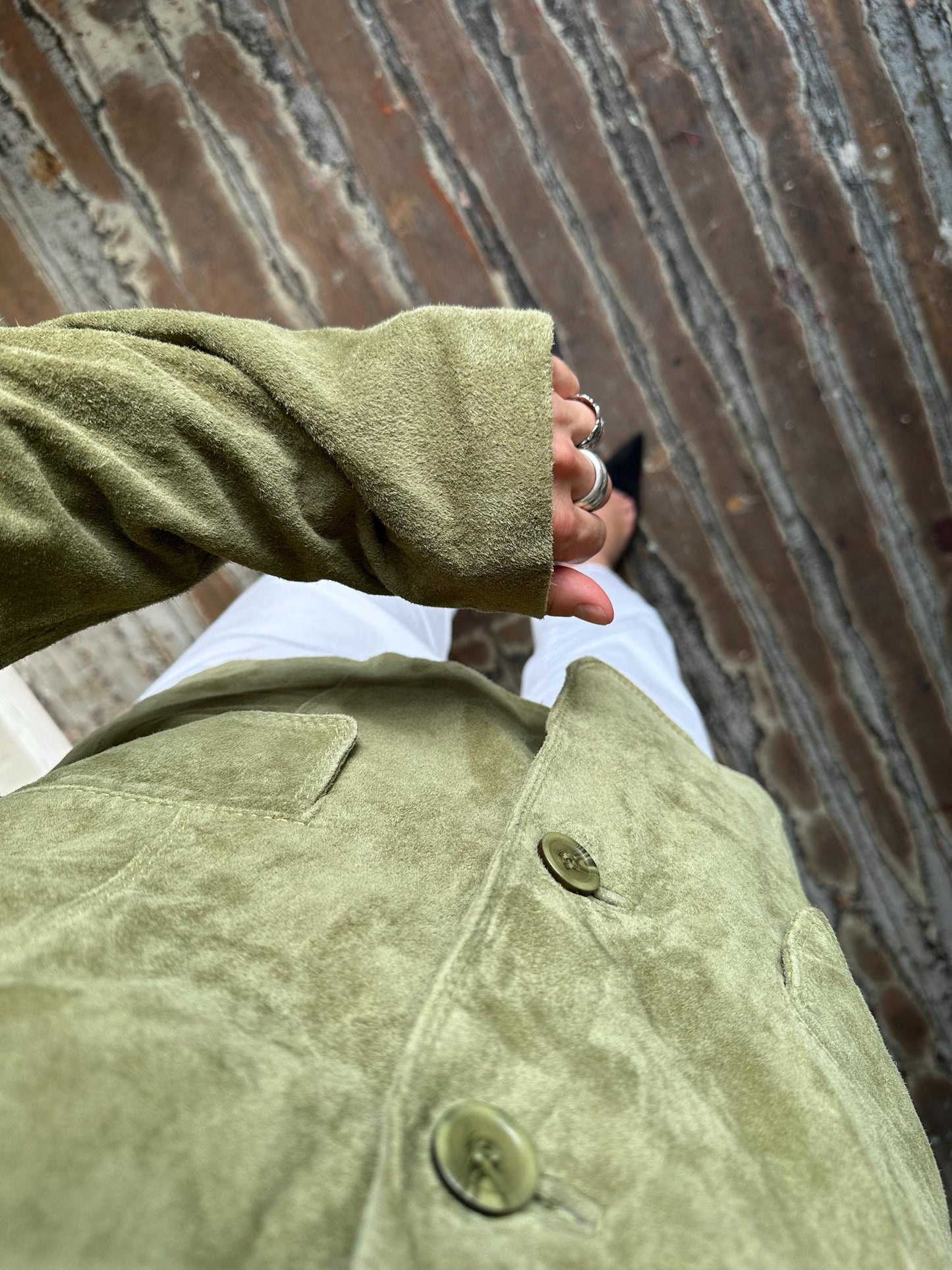 A person wearing a green jacket with their arm extended, standing in front of a brick wall.