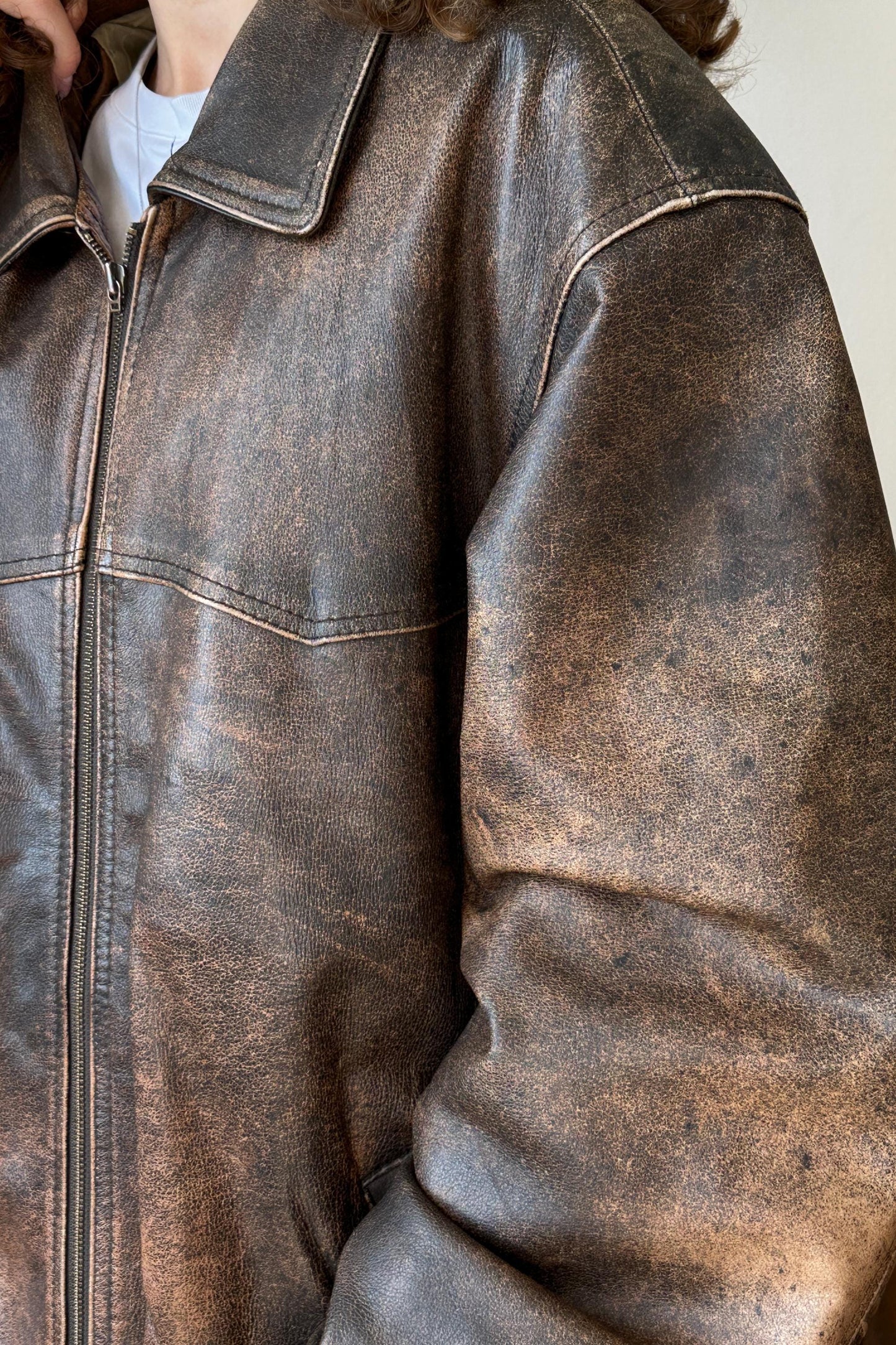 A close-up view of a worn, brown leather jacket with visible signs of aging, such as cracks and stains.