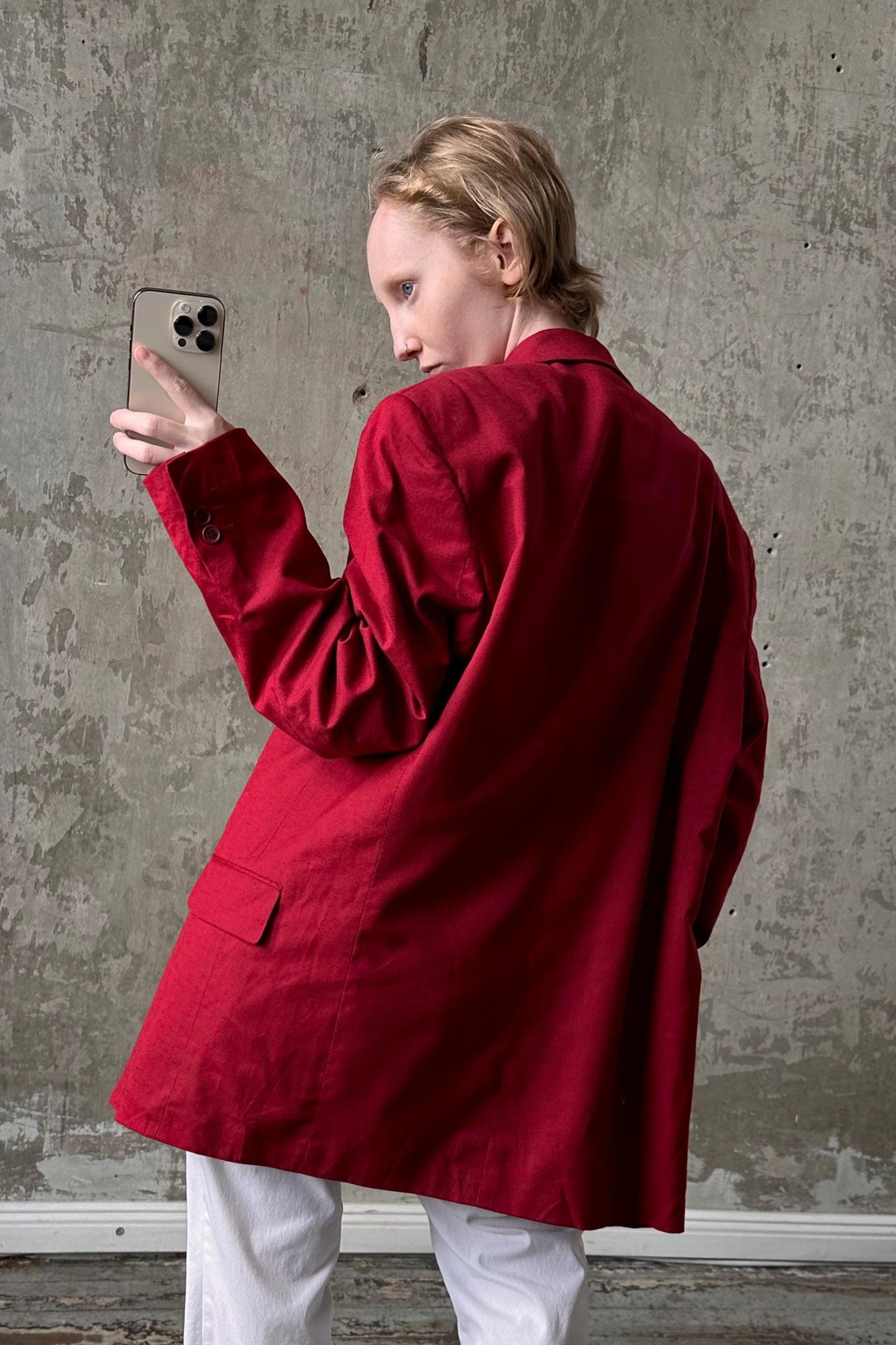 A person wearing a red jacket is holding a smartphone and looking at it, with a concrete wall in the background.