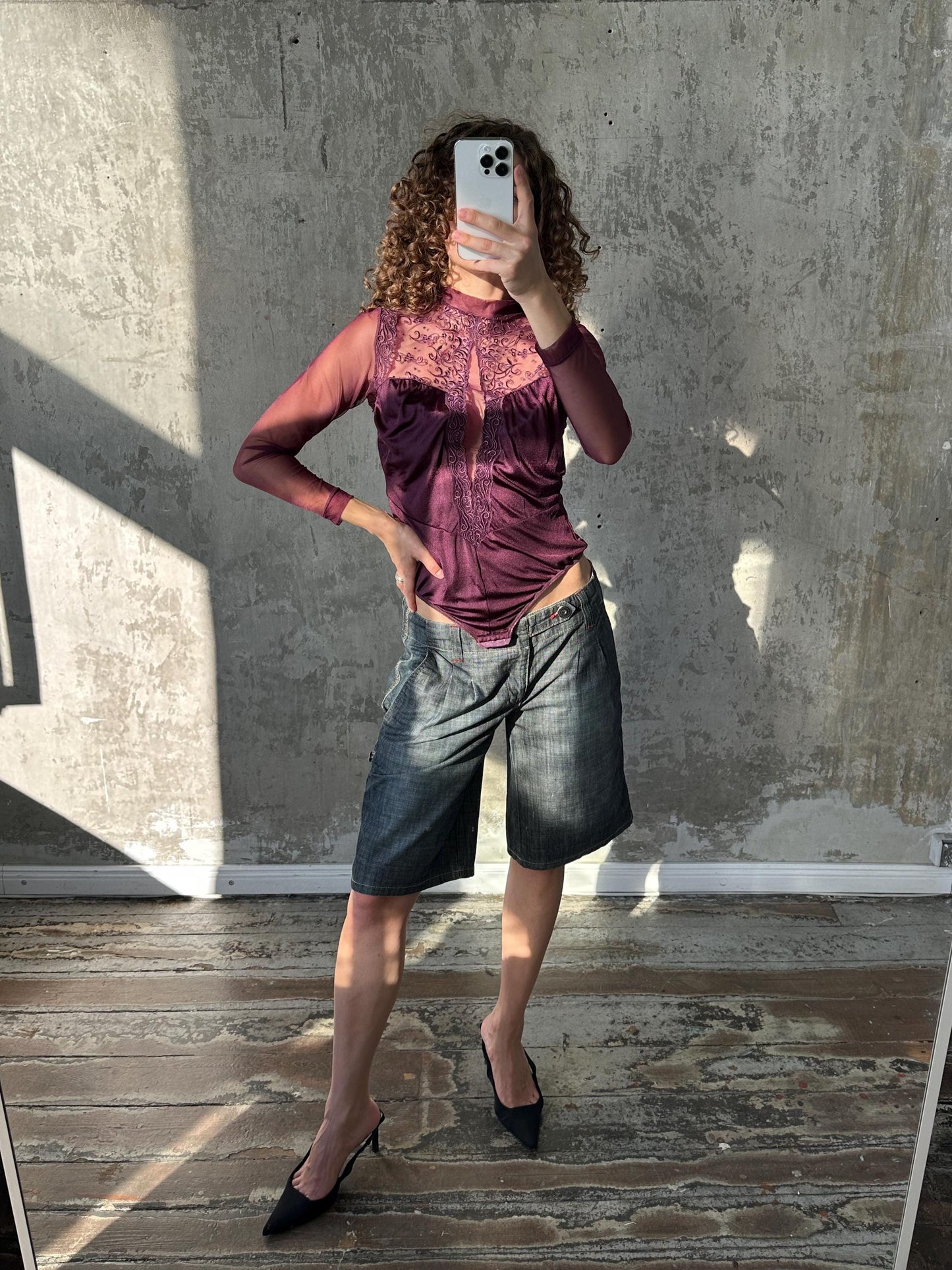 A woman is taking a selfie in front of a concrete wall, holding a smartphone in her hand.