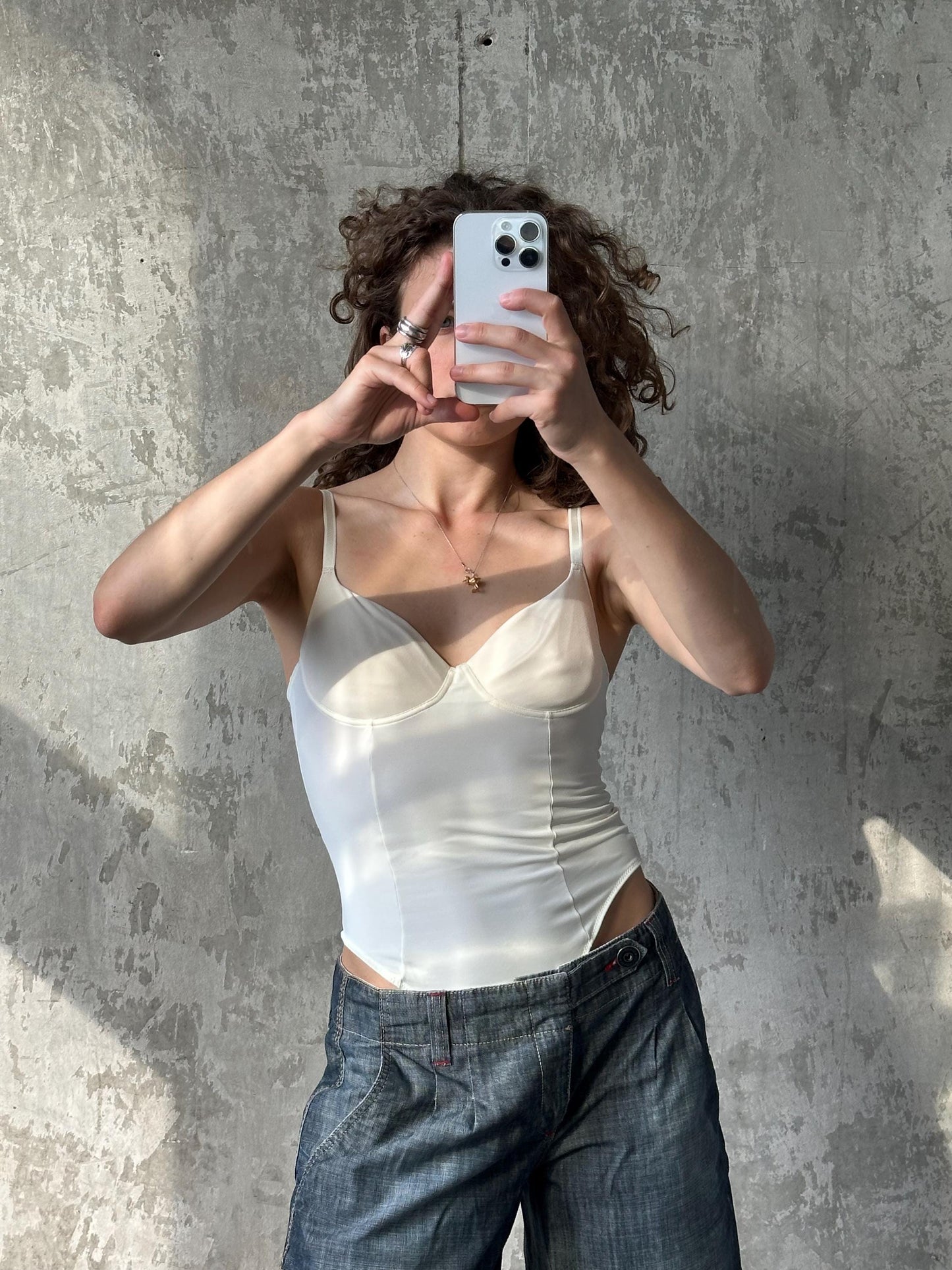 A woman is taking a selfie with her phone, holding it up to her face against a textured gray wall.