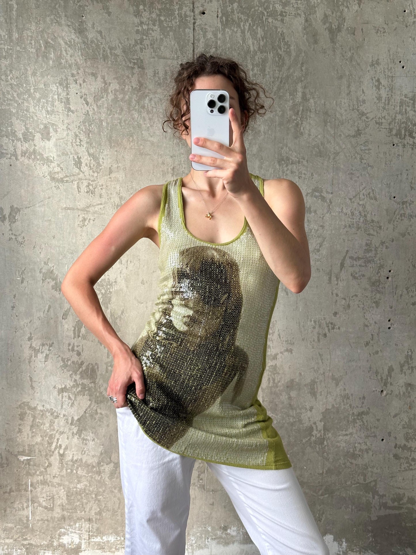 A person is taking a selfie with a smartphone, holding the device up to their face against a concrete wall background.
