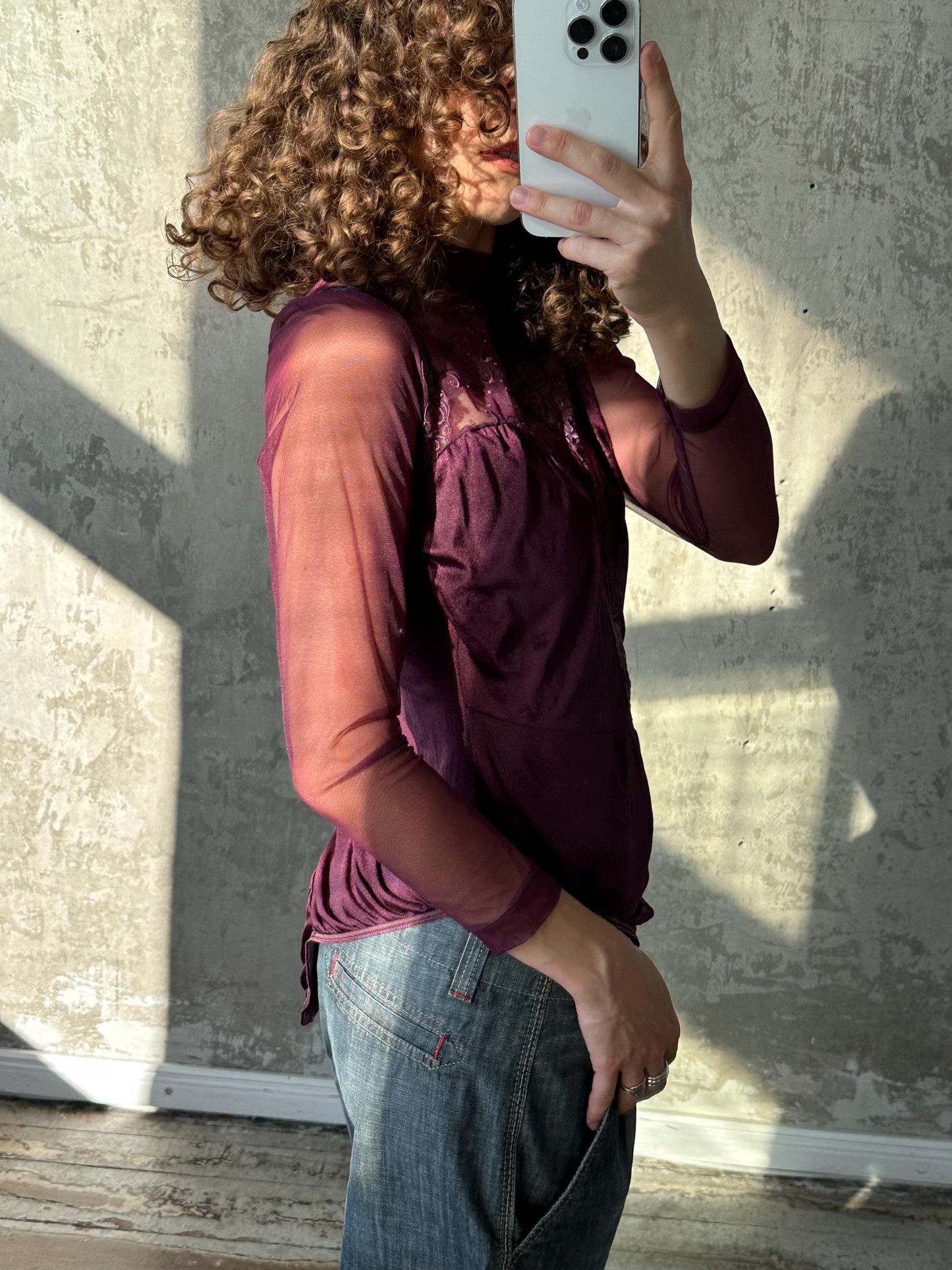 A person with curly hair is taking a selfie with a smartphone, holding the phone up to their face to capture the image.
