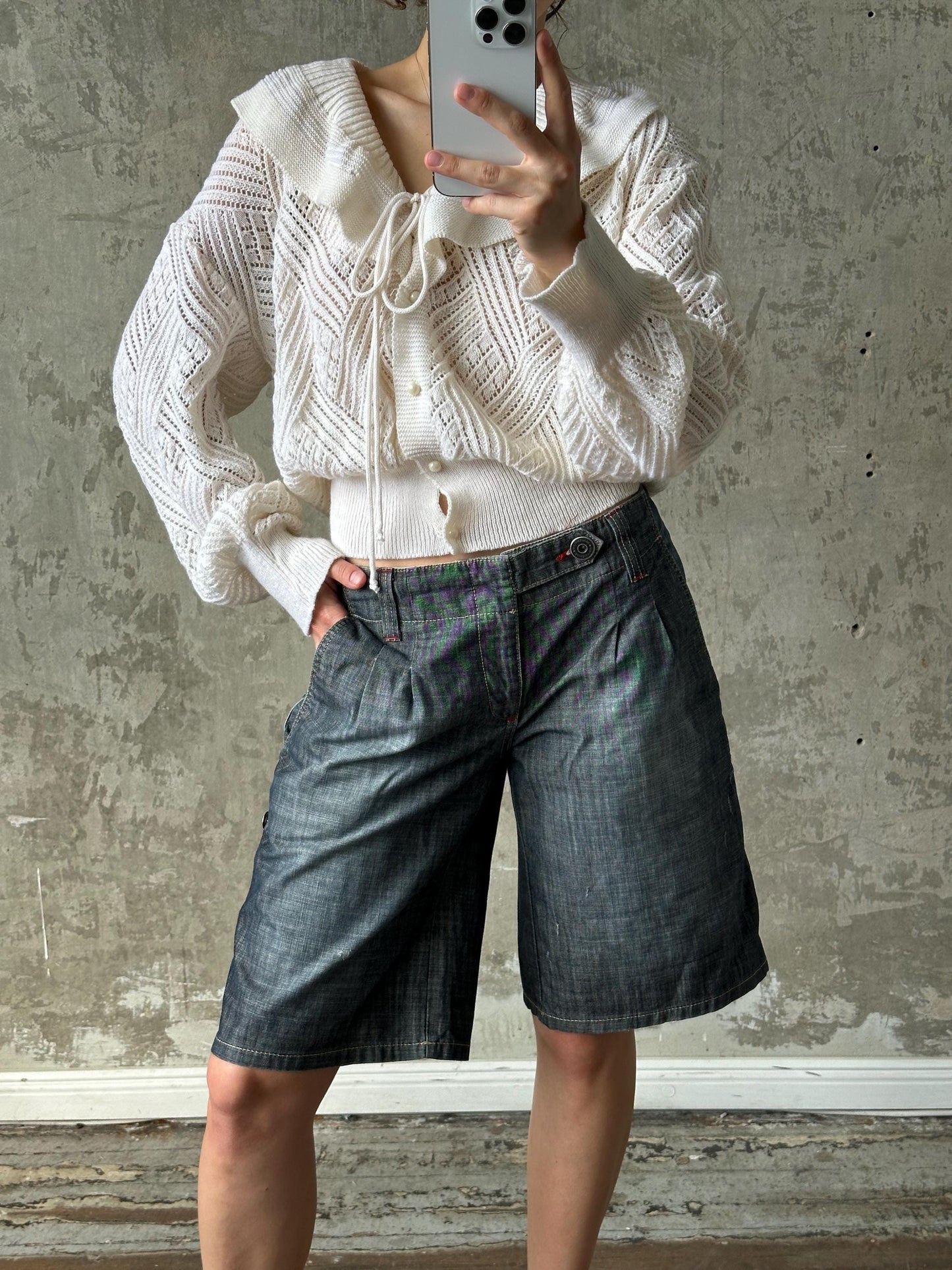 A person is taking a selfie with a white sweater and blue jeans, holding a smartphone in their hand.