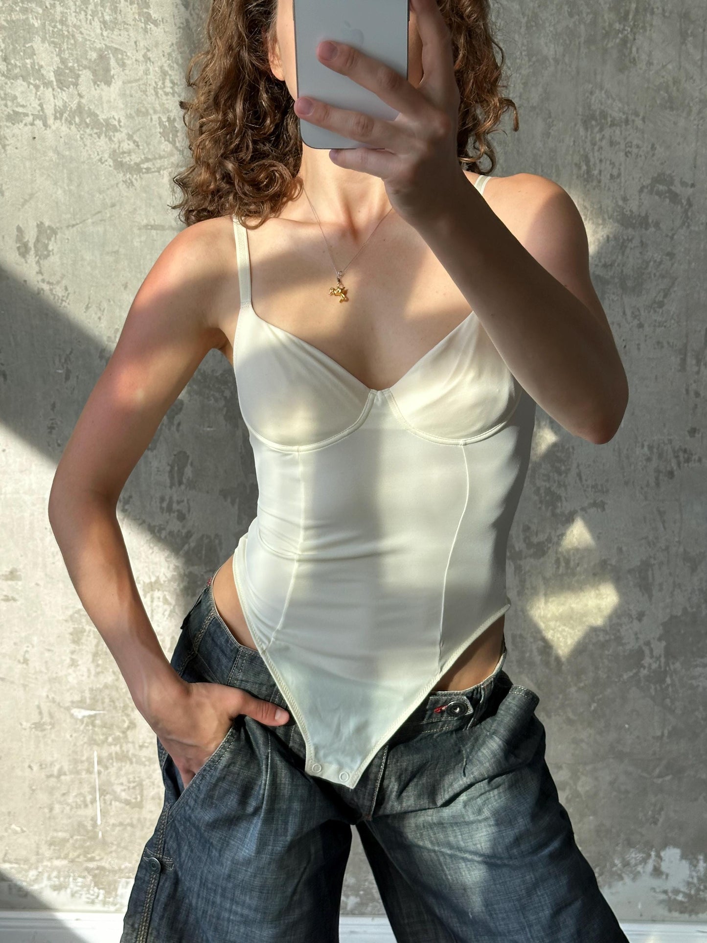 A woman is taking a selfie with a smartphone, wearing a white top and blue jeans.