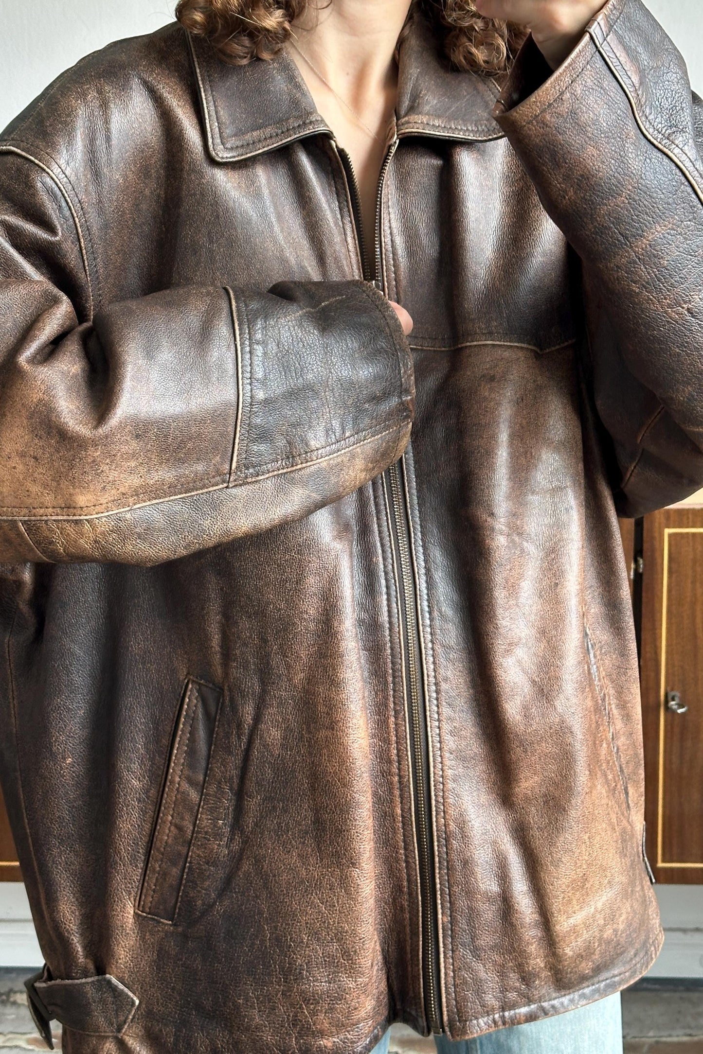 A person wearing a brown leather jacket with a zipper and a collar.