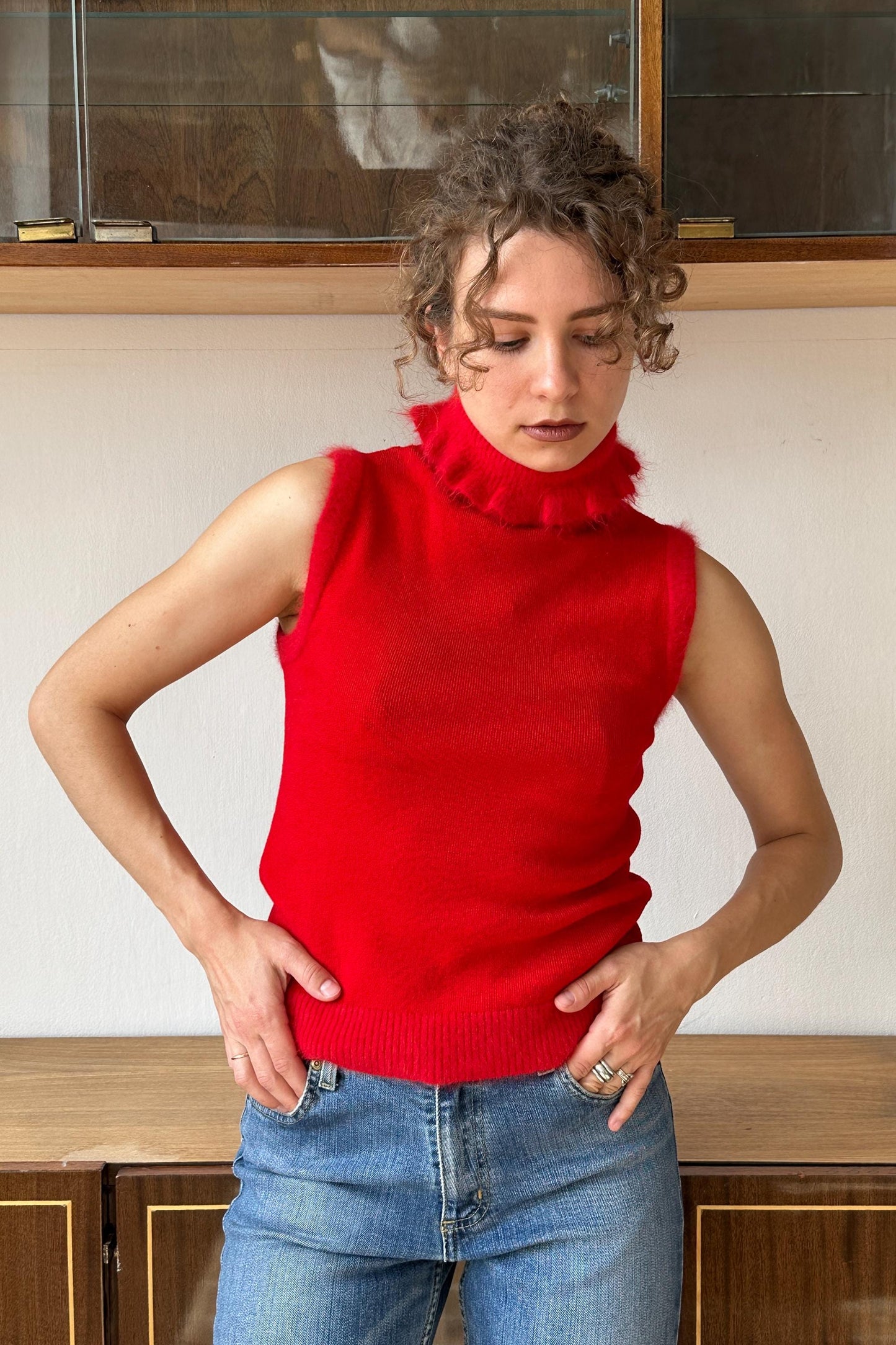 A woman wearing a red sleeveless top and blue jeans stands in front of a glass display case.