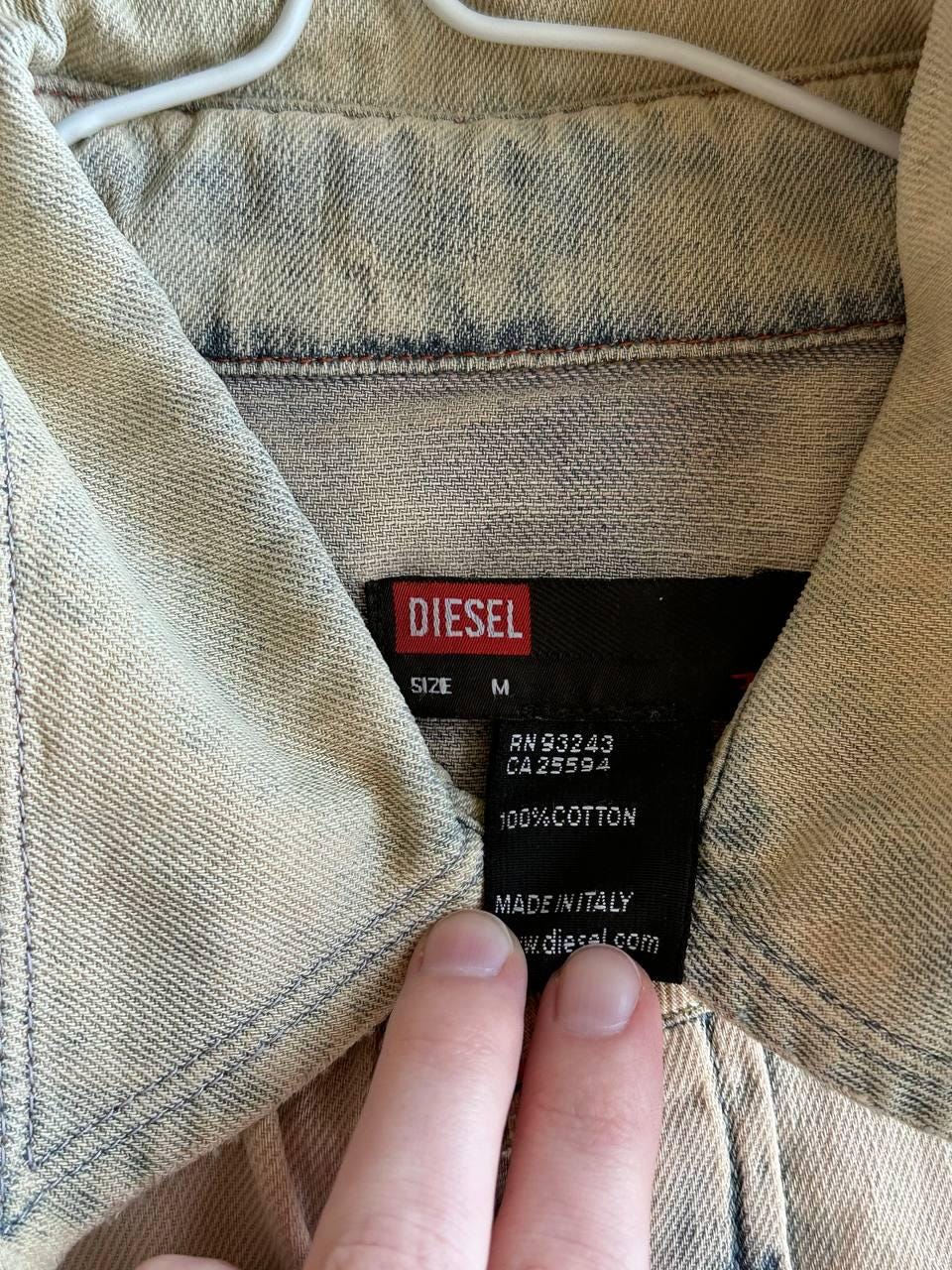 a close-up view of a denim jacket, with a label attached to the collar. The label appears to be a size label from the brand Diesel, indicating the size M.