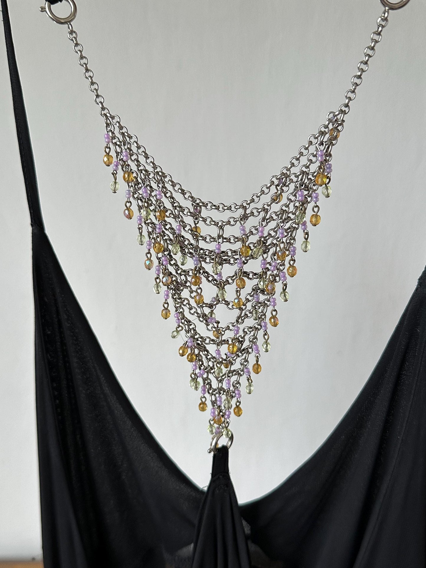 A close-up view of a black dress with a silver chain necklace featuring a cascading arrangement of small, colorful beads.
