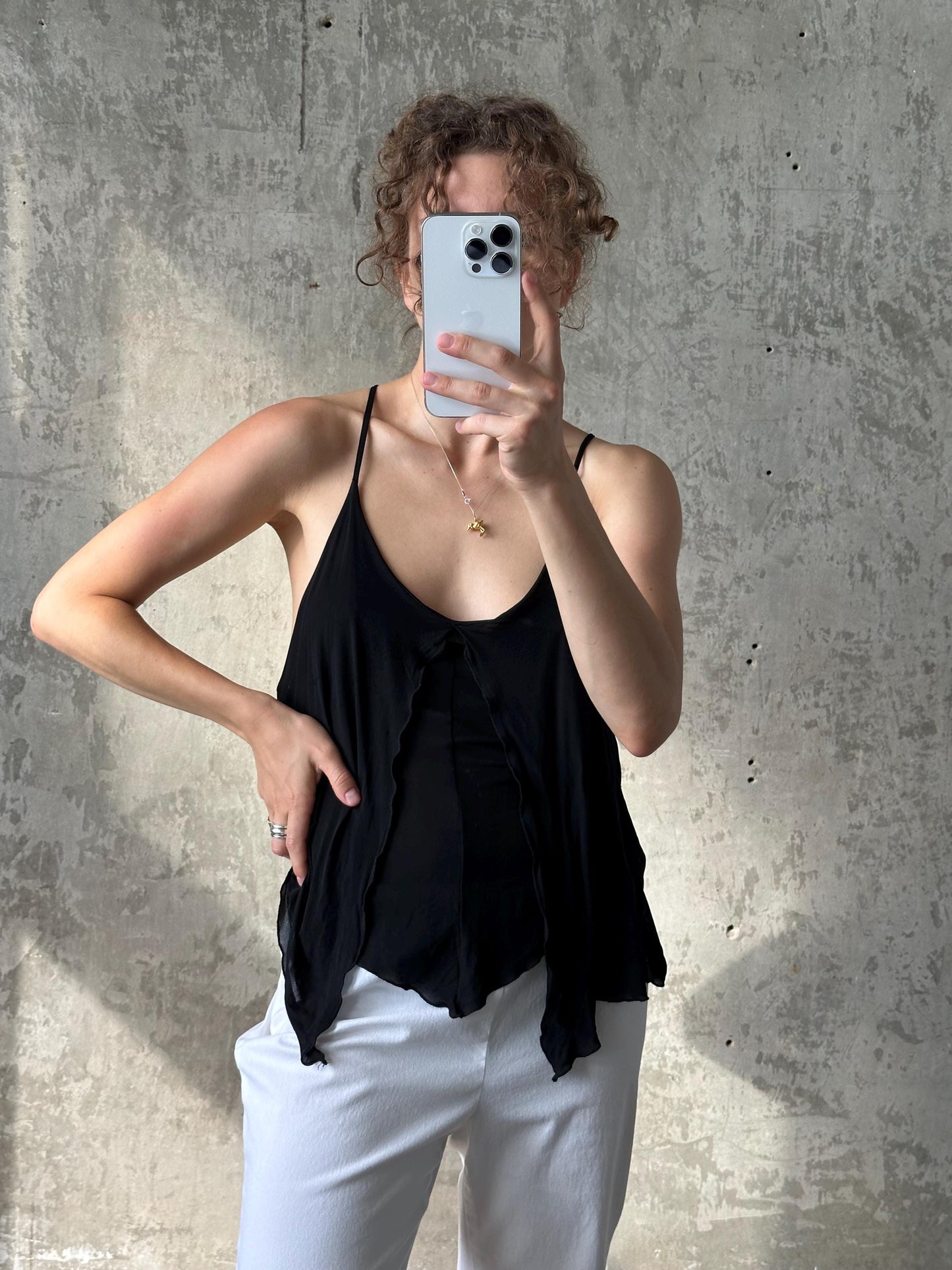 A woman is taking a selfie with her iPhone, holding it up to her face against a concrete wall background.