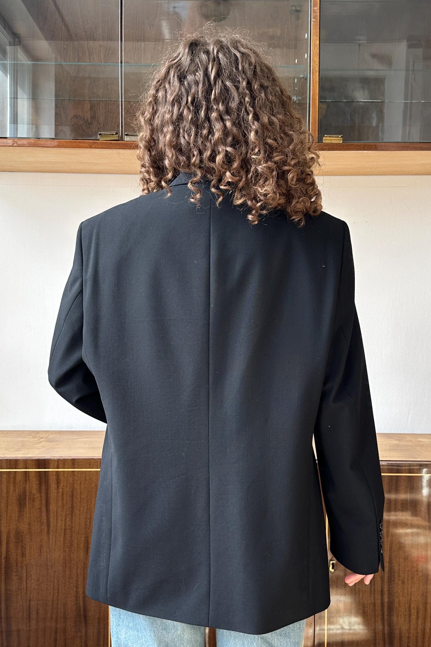 the back of a person wearing a black blazer, with their curly hair visible.