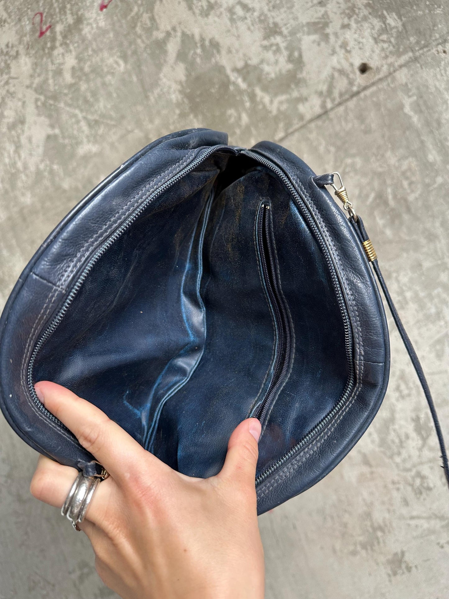 A hand holding a black leather handbag with a zipper closure.