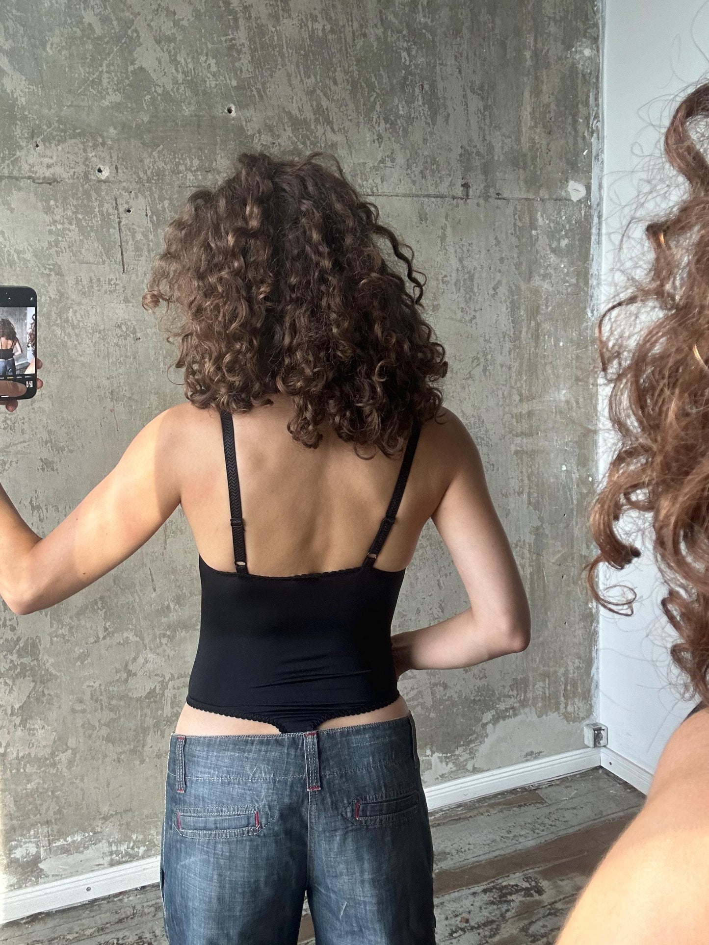 a person with curly hair taking a selfie in front of a concrete wall.