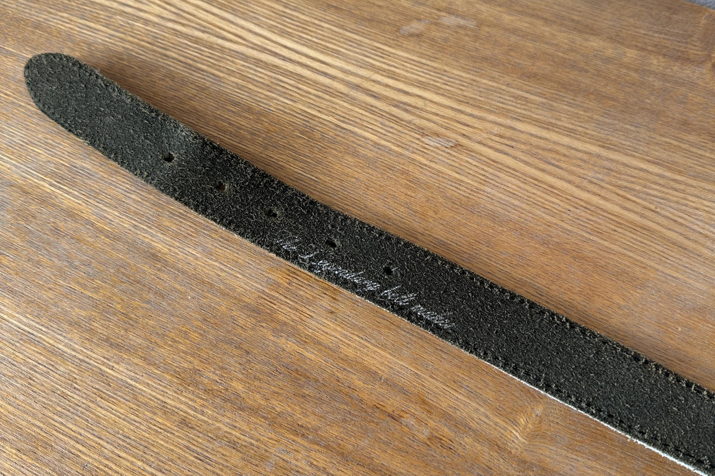 A black leather belt with a metal buckle is lying on a wooden surface.