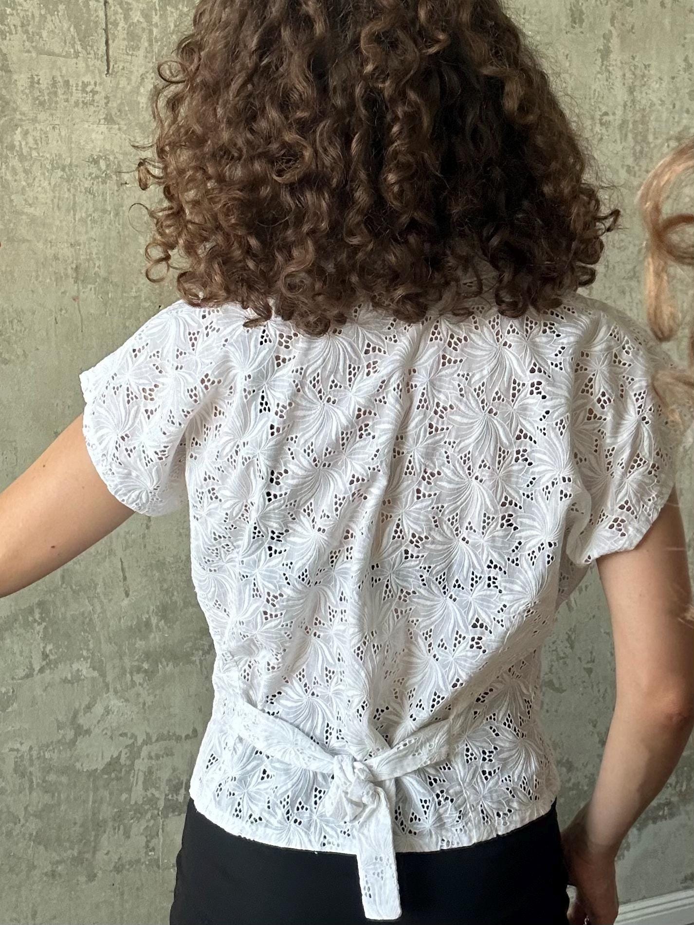 the back view of a woman wearing a white lace blouse with a floral pattern.