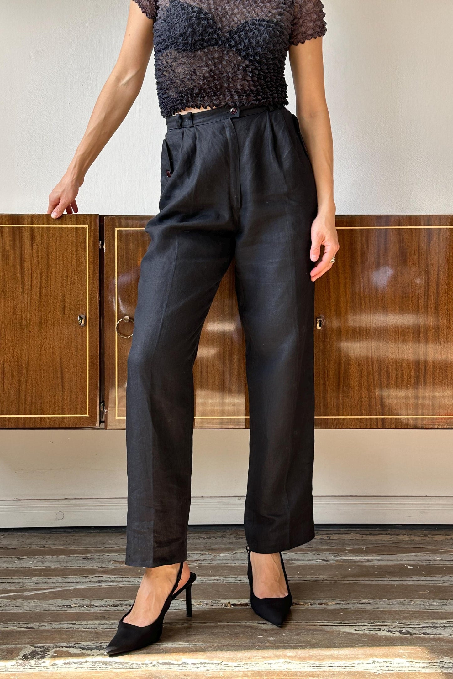 A woman wearing a black top and black pants stands in front of a wooden cabinet.