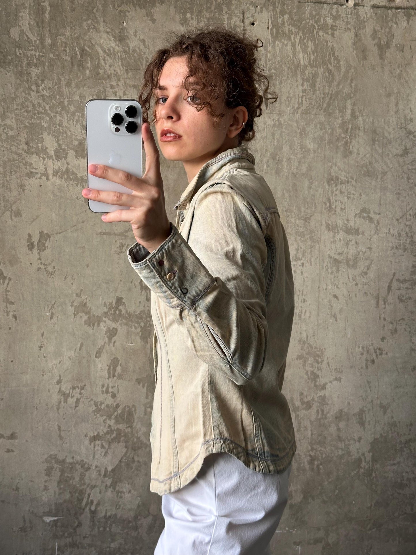 A person is taking a selfie with a smartphone, holding it up to their face against a concrete wall background.