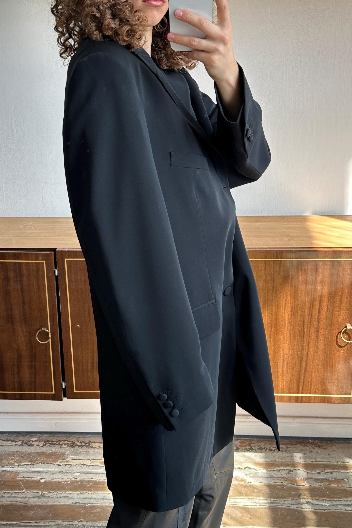 A person taking a selfie with a black blazer in a room with wooden cabinets.
