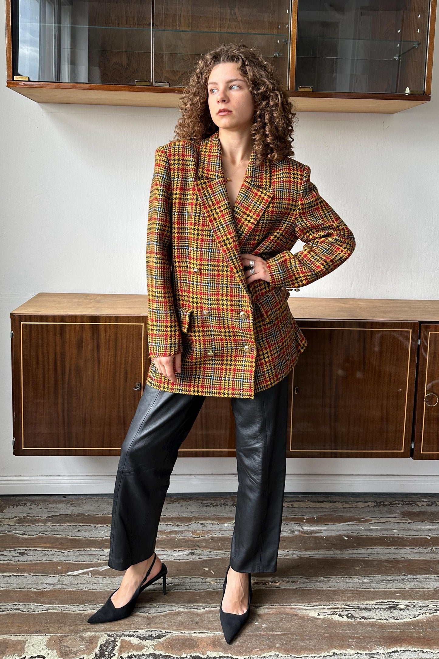 A woman wearing a plaid jacket and black pants stands in a room with wooden cabinets in the background.